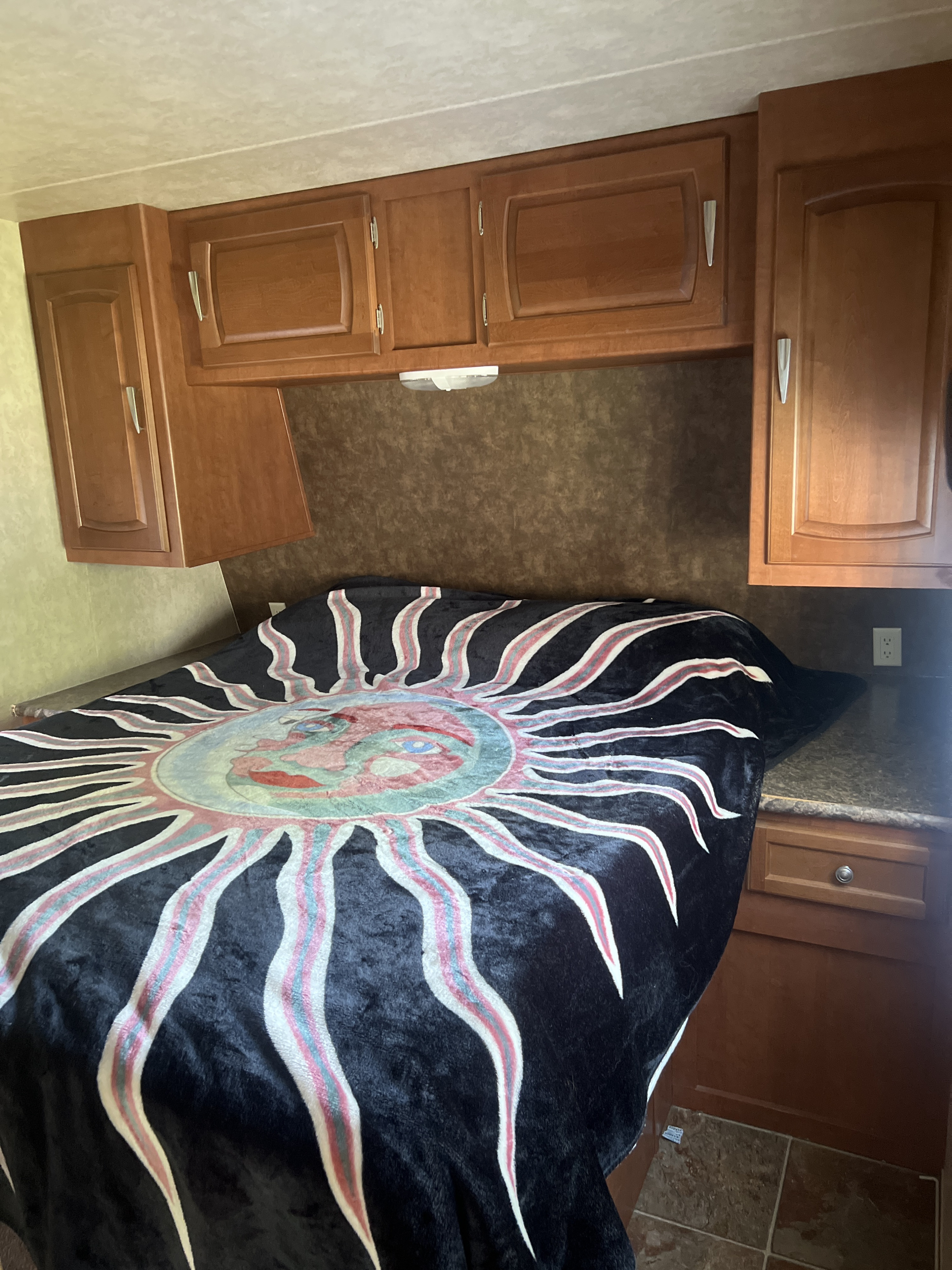 RV rental bedroom featuring wooden overhead cabinets, a dark backsplash, and a cozy bed with a vibrant sun blanket.. Forest River Evo 2013