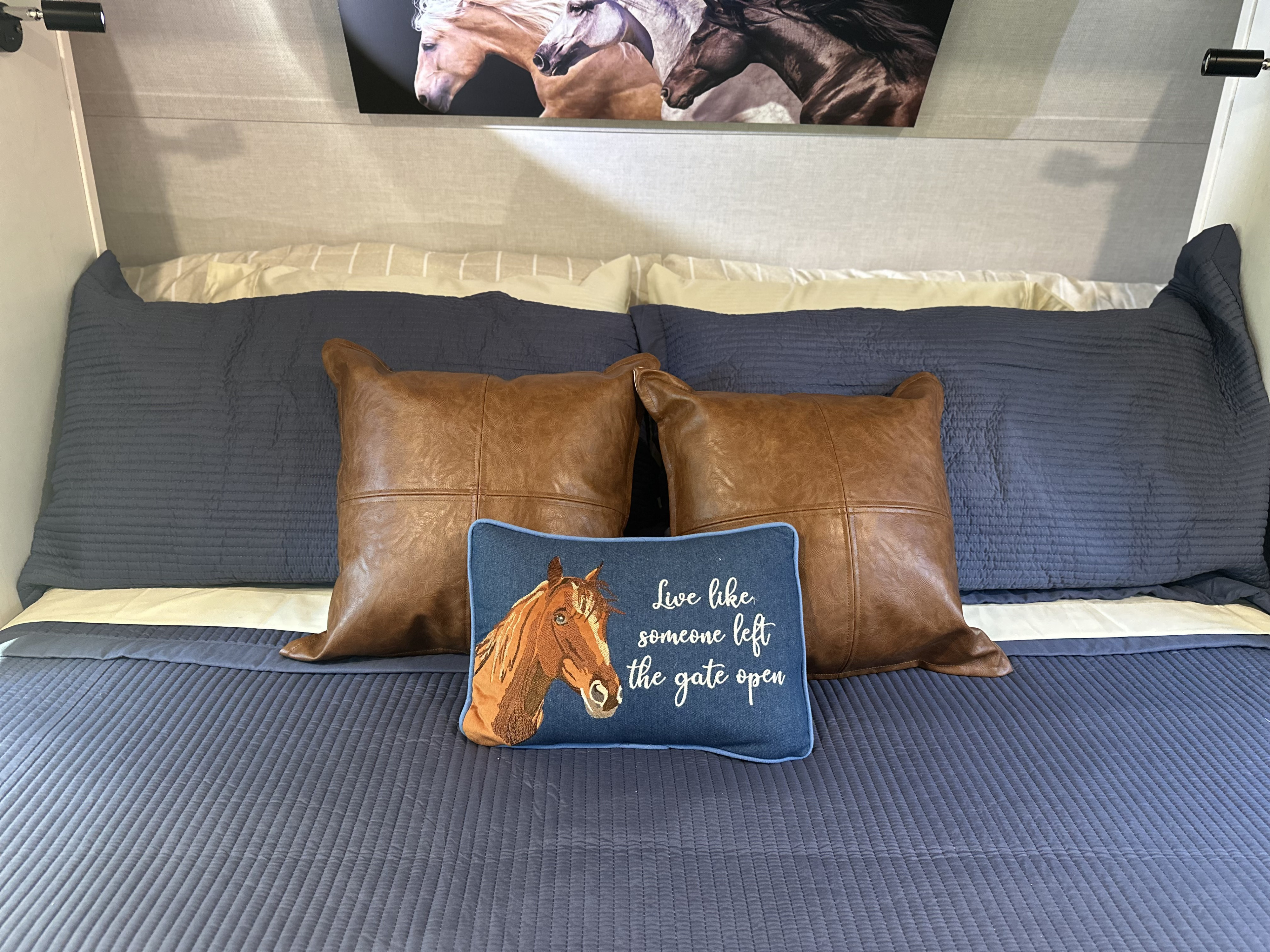 Cozy rv rental bed features quilted blue bedding, faux-leather pillows, and a horse-themed cushion with an inspiring quote.. Forest River Vibe 2026