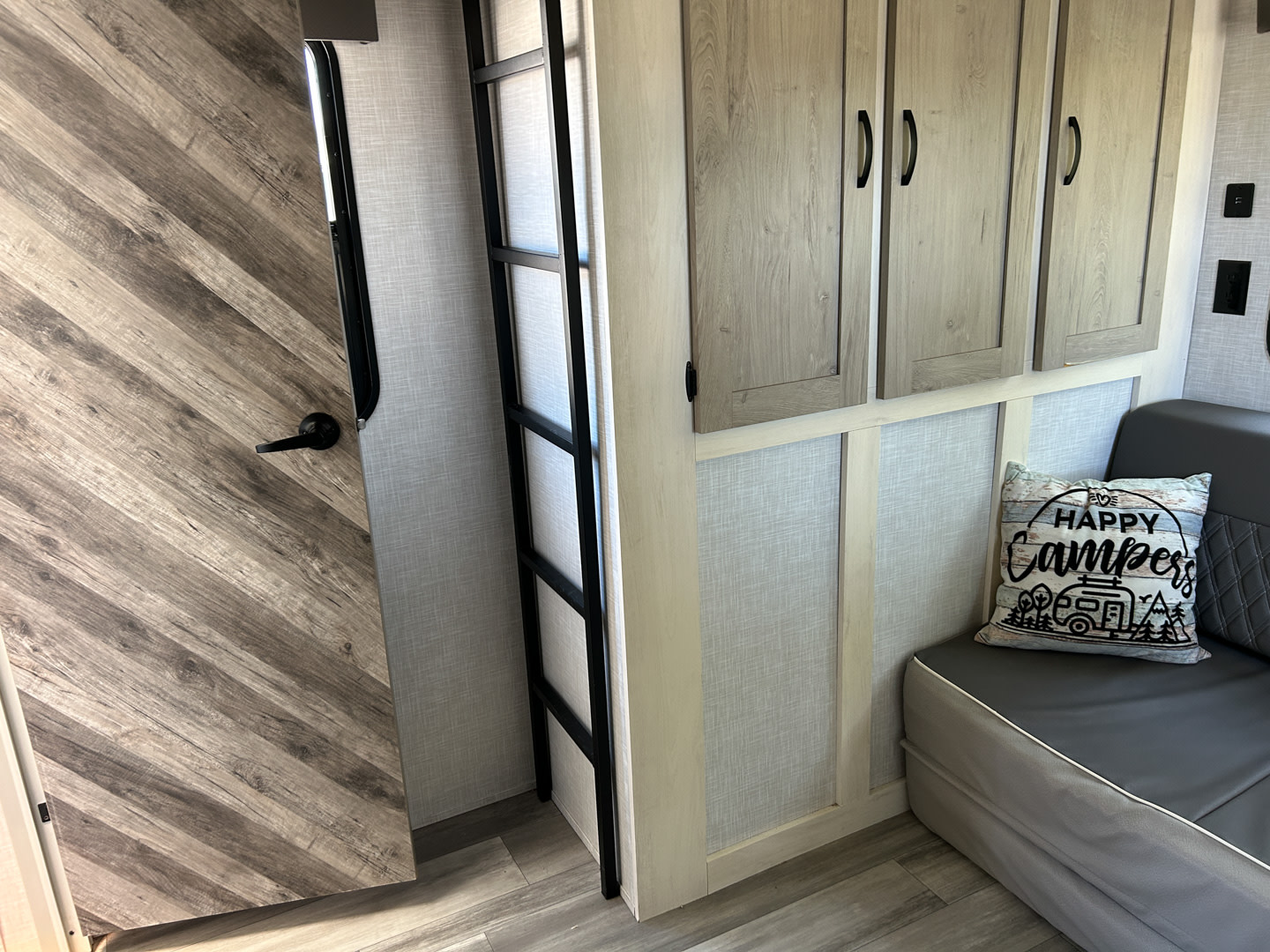 Inside an RV rental: a wood-look door, ladder, storage cabinets, and a comfy bench with a fun "Happy Campers" pillow.. Forest River Impression 2022