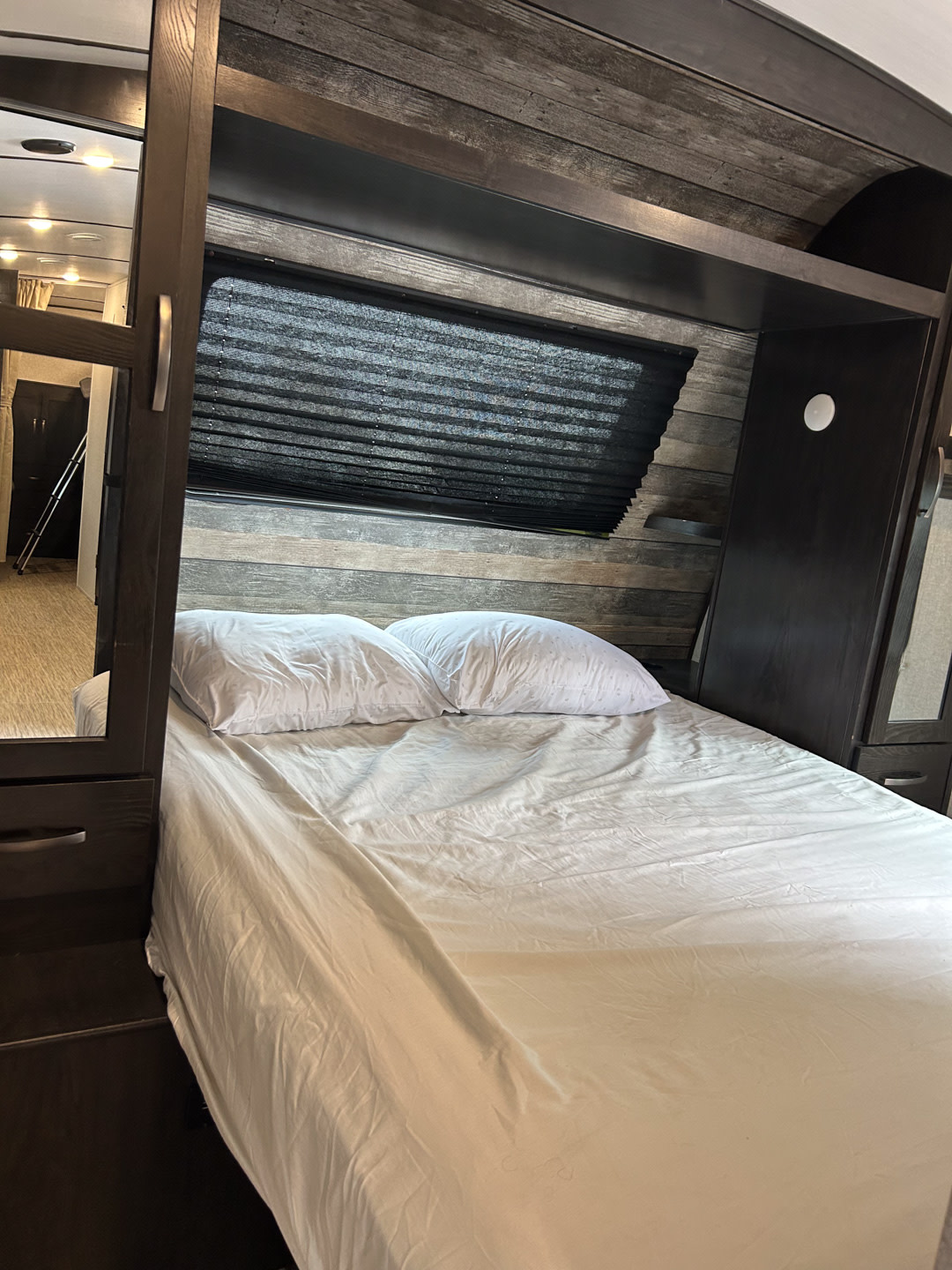 RV rental bedroom with a cozy bed, dark wood-paneled walls, and privacy blinds. Ideal travel accommodation.. Surveyor Legend 2021