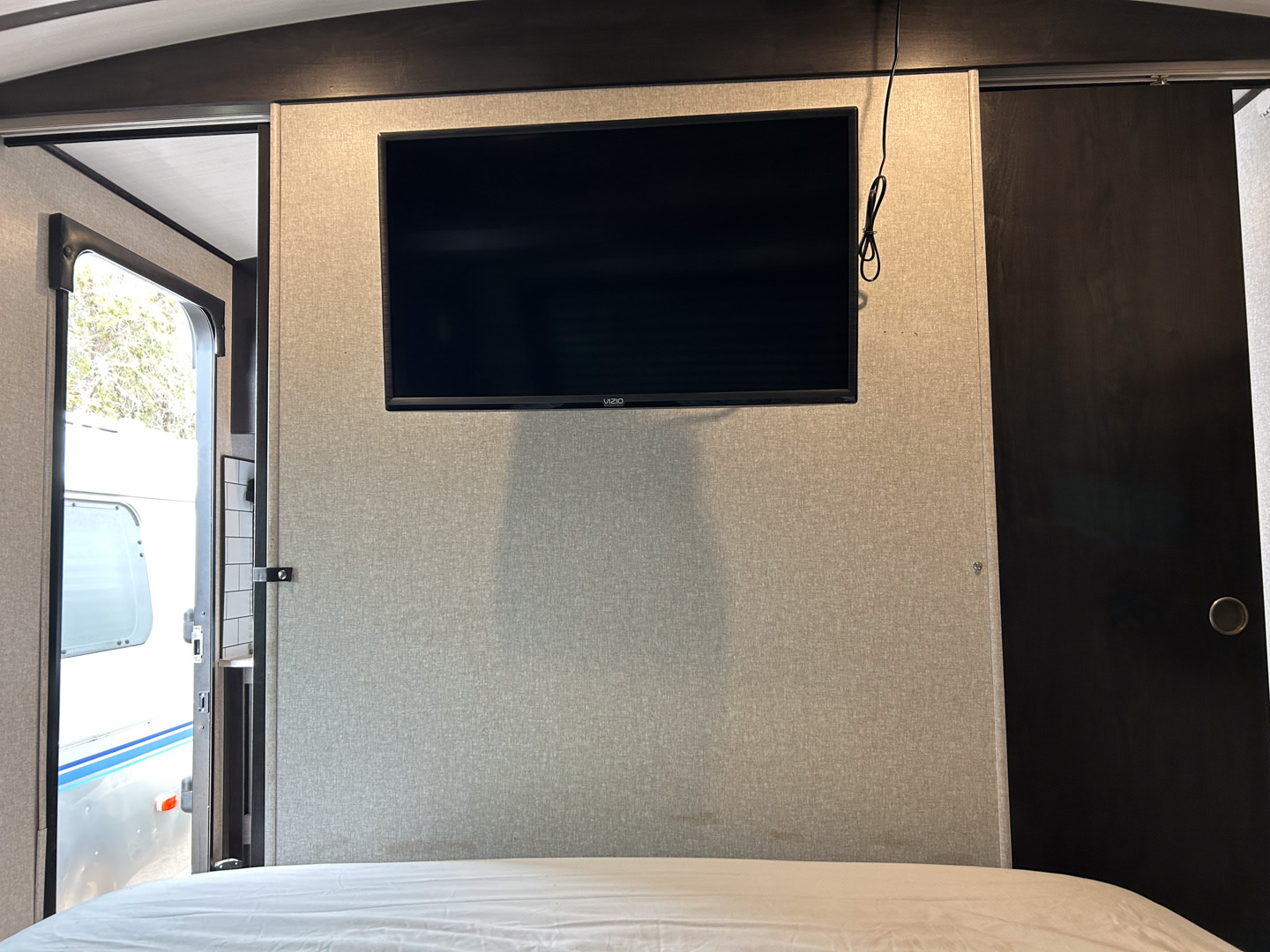 RV rental bedroom: Mounted TV above a white bed, open door on left showing outside, dark sliding door on right.. Surveyor Legend 2021