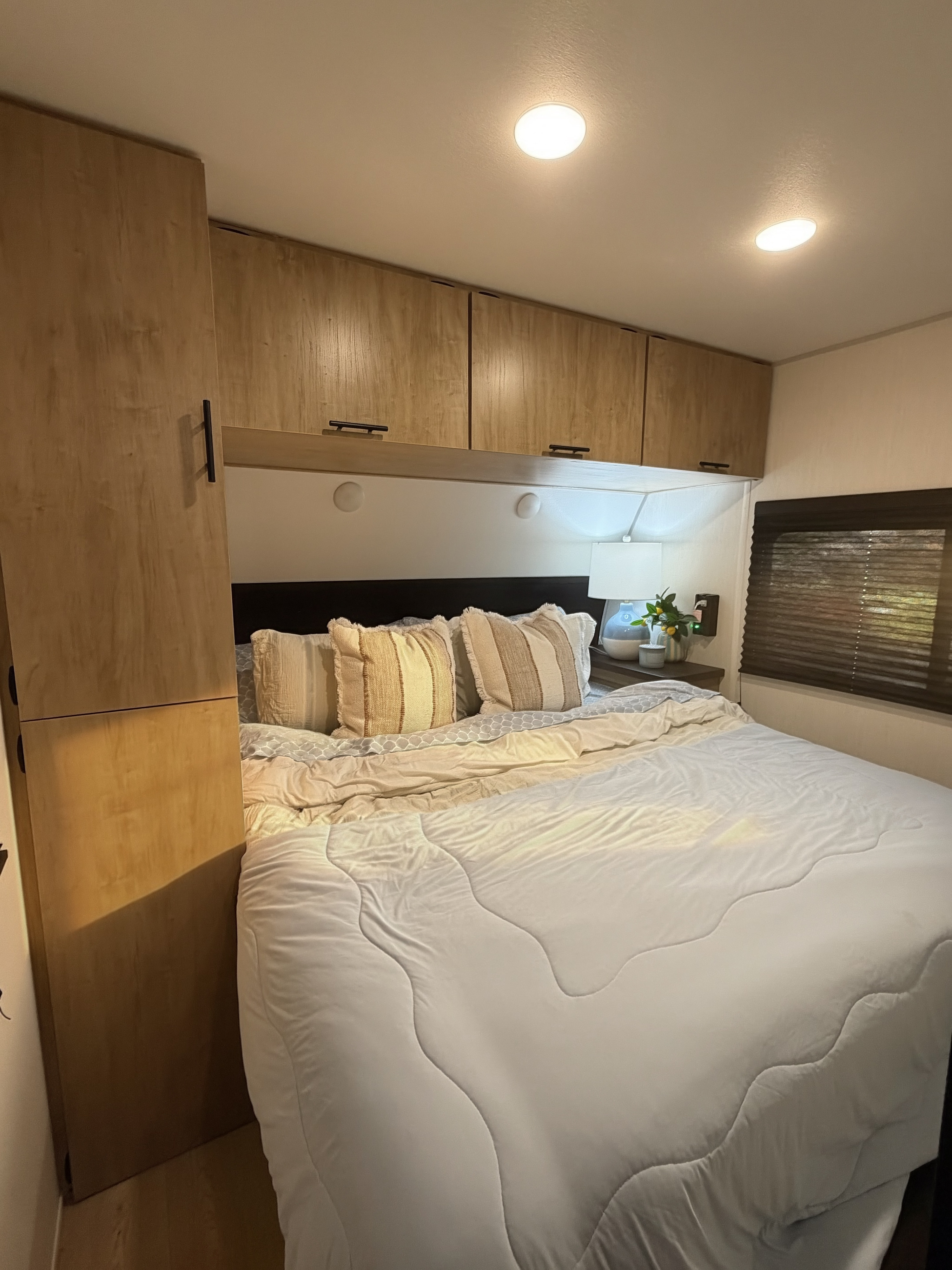 Cozy RV rental bedroom featuring a comfy bed, overhead cabinets, and soft lighting, ideal for a relaxing stay.. Forest River CHEROKEE WOLF DEN 301BH 2026