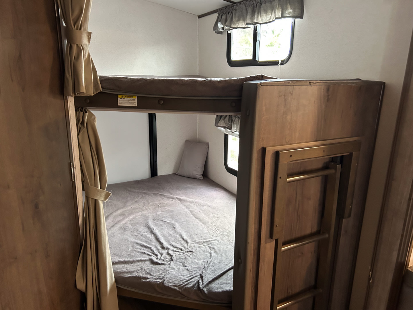 RV rental bunk beds featuring gray bedding, privacy curtains, and a stored ladder for easy access.. Keystone RV Passport 2021
