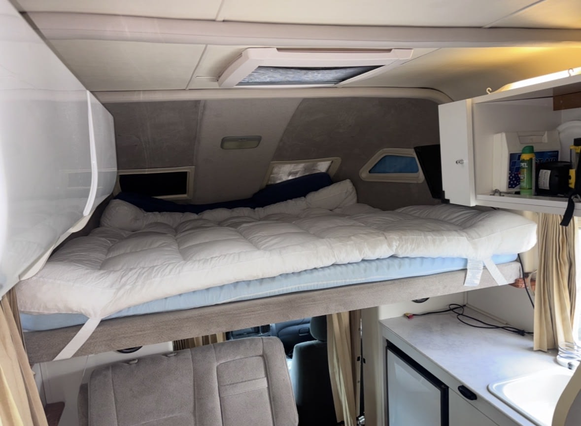 RV rental interior featuring a cozy elevated bed over the cab, storage, and kitchenette. Perfect for compact campervan travel.. 5TBKT44114S447491 Toyota Tundra Excruiser 2004