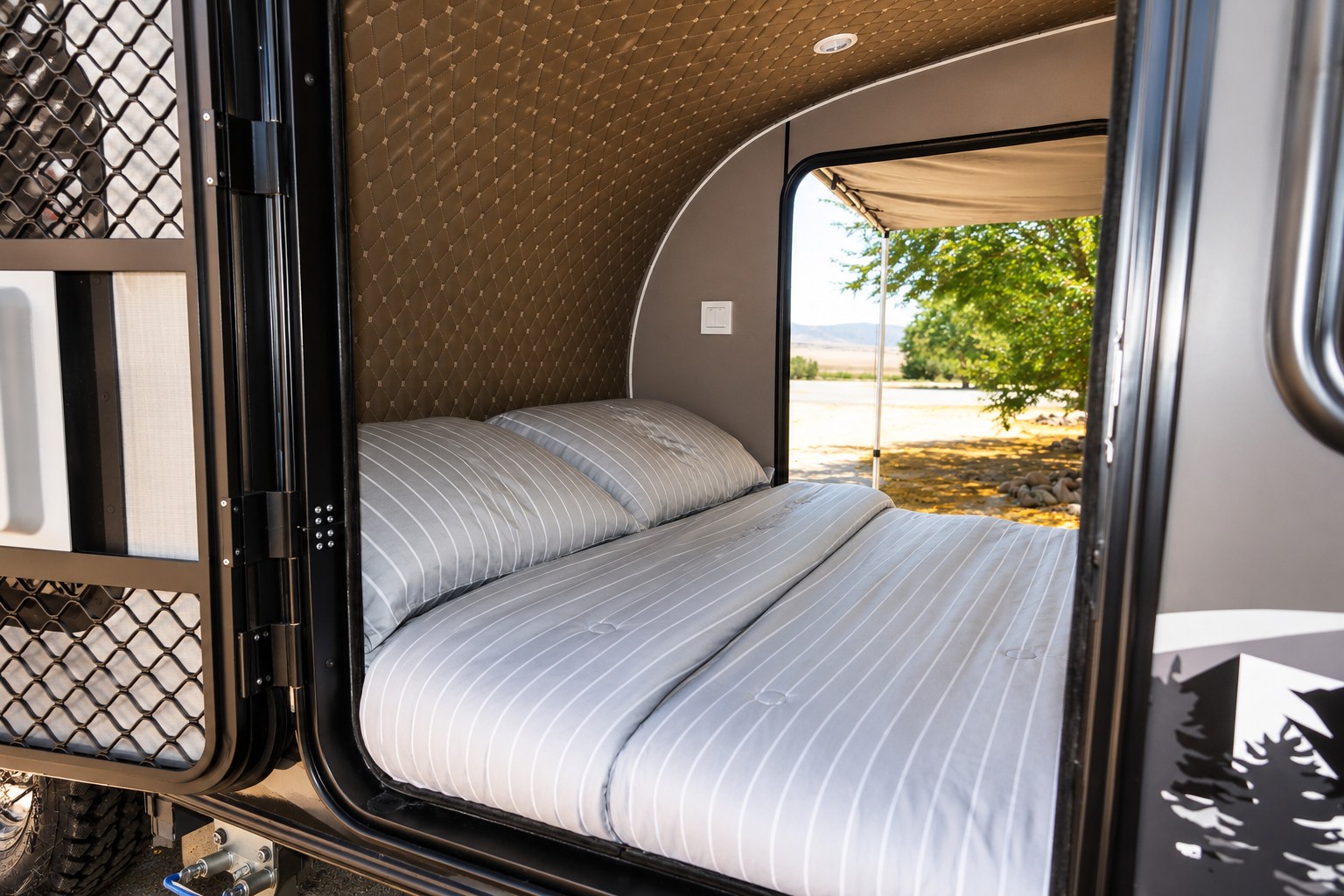 Cozy RV rental bedroom with striped bedding and open door offering scenic outdoor views, perfect for your next adventure.. Beyond Outdoors MiniGrey 2025