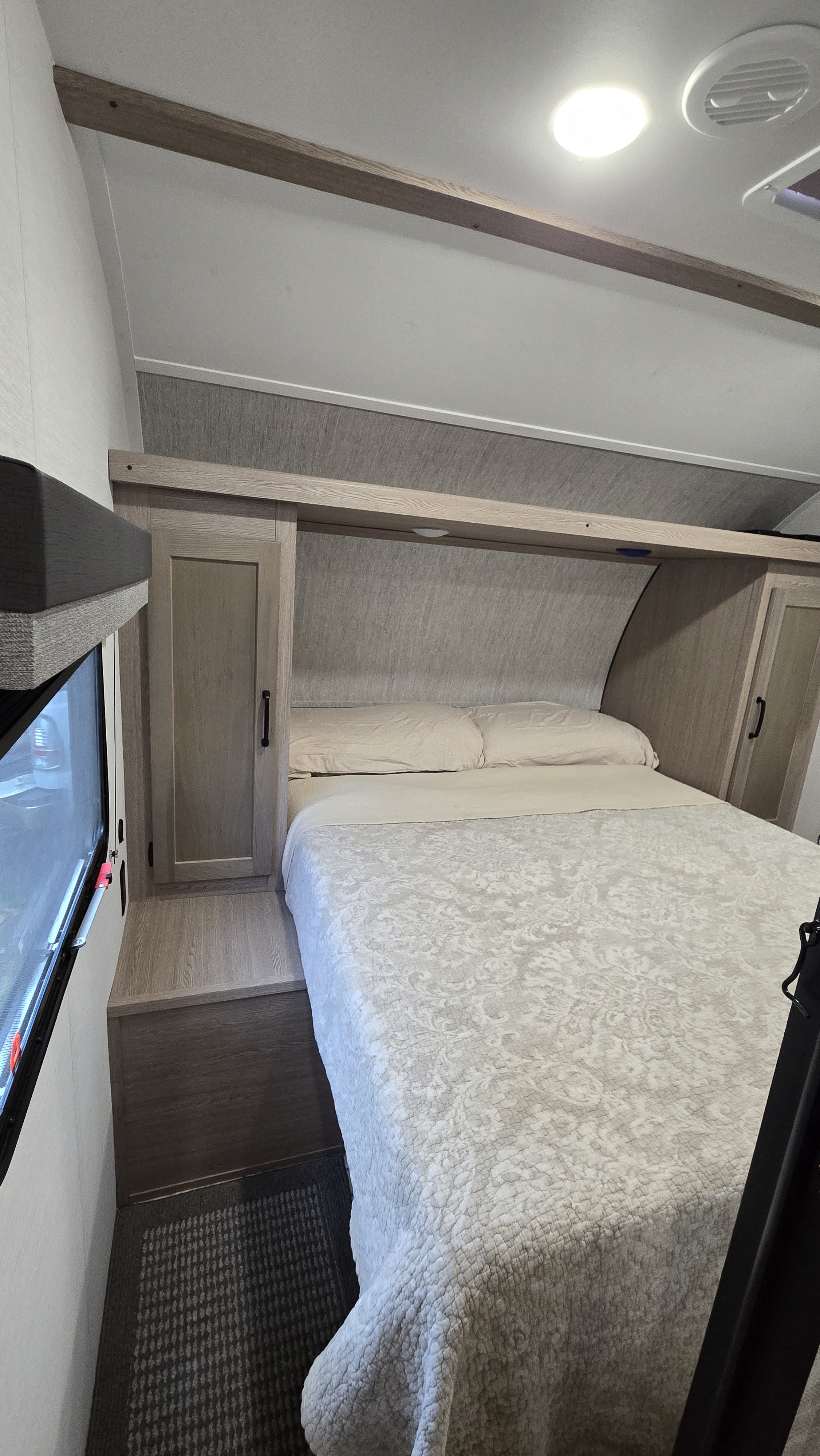 RV rental bedroom: a queen bed with light quilted bedding, wood-look cabinets, and a side window for light.. Gulf Stream Ameri-Lite 2025