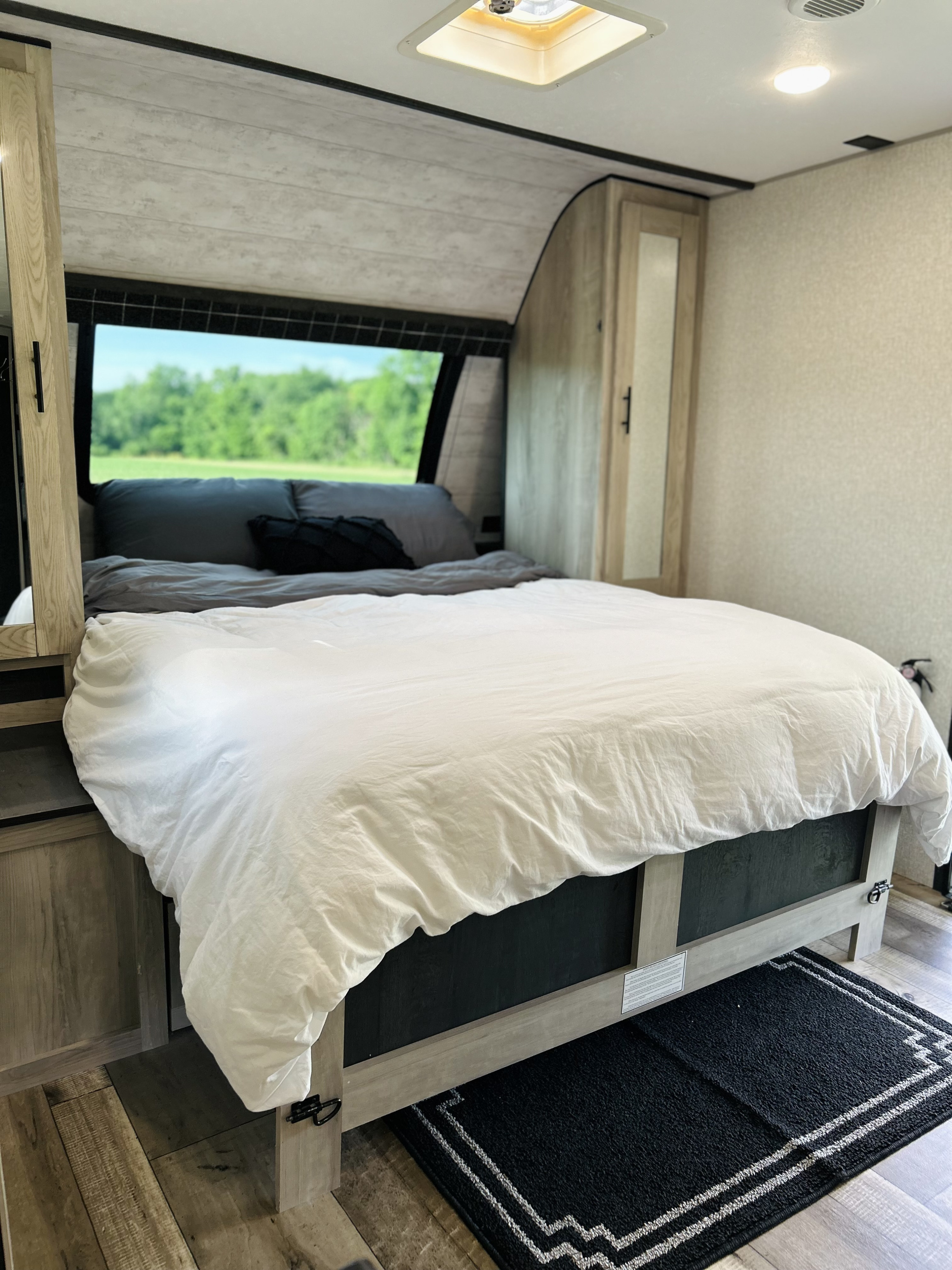 RV rental bedroom features a made bed, wide window with green nature view, light wood cabinetry, and wood-pattern floor.. KZ Connect C231BHKSE 2023