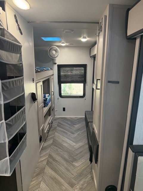 Modern RV rental interior, showing a bright hallway with herringbone floor, bunk beds on left, window, and fan.. Heartland RVs Mallard 2023