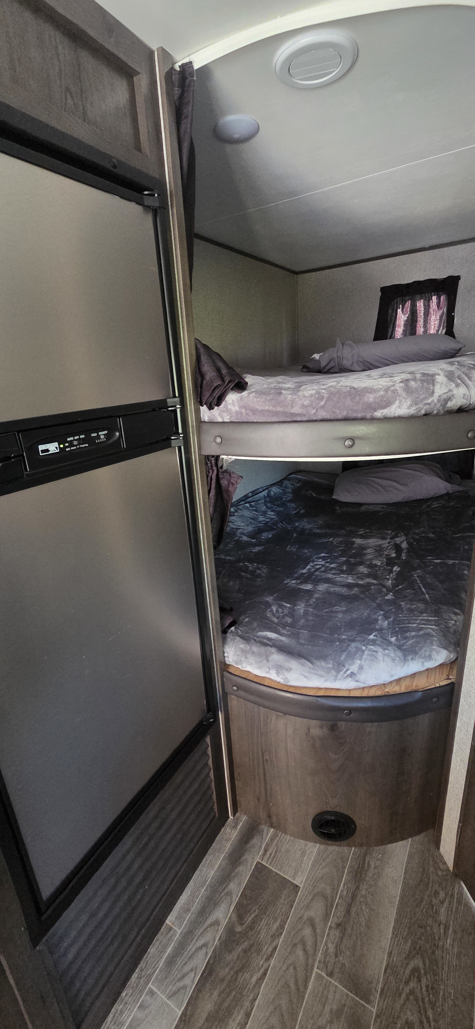 RV rental interior: A silver refrigerator stands next to bunk beds, featuring purple and grey blankets, and wood-look flooring.. Jayco Jay Flight SLX 2021