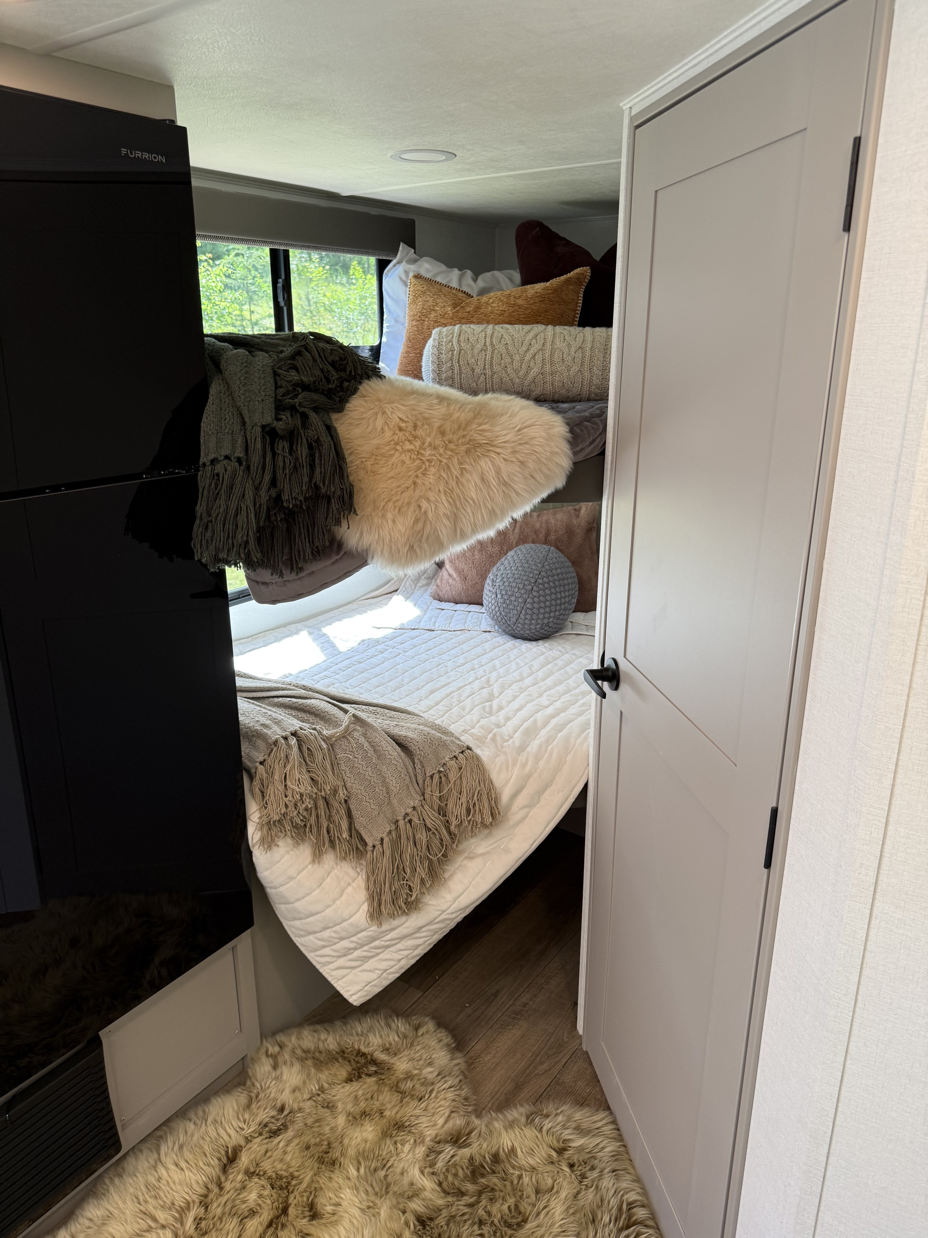 This cozy RV rental bedroom features a comfy bed with decorative pillows and blankets, a Furrion appliance, and a modern light-toned door.. Alliance Delta Solo BH181 2026
