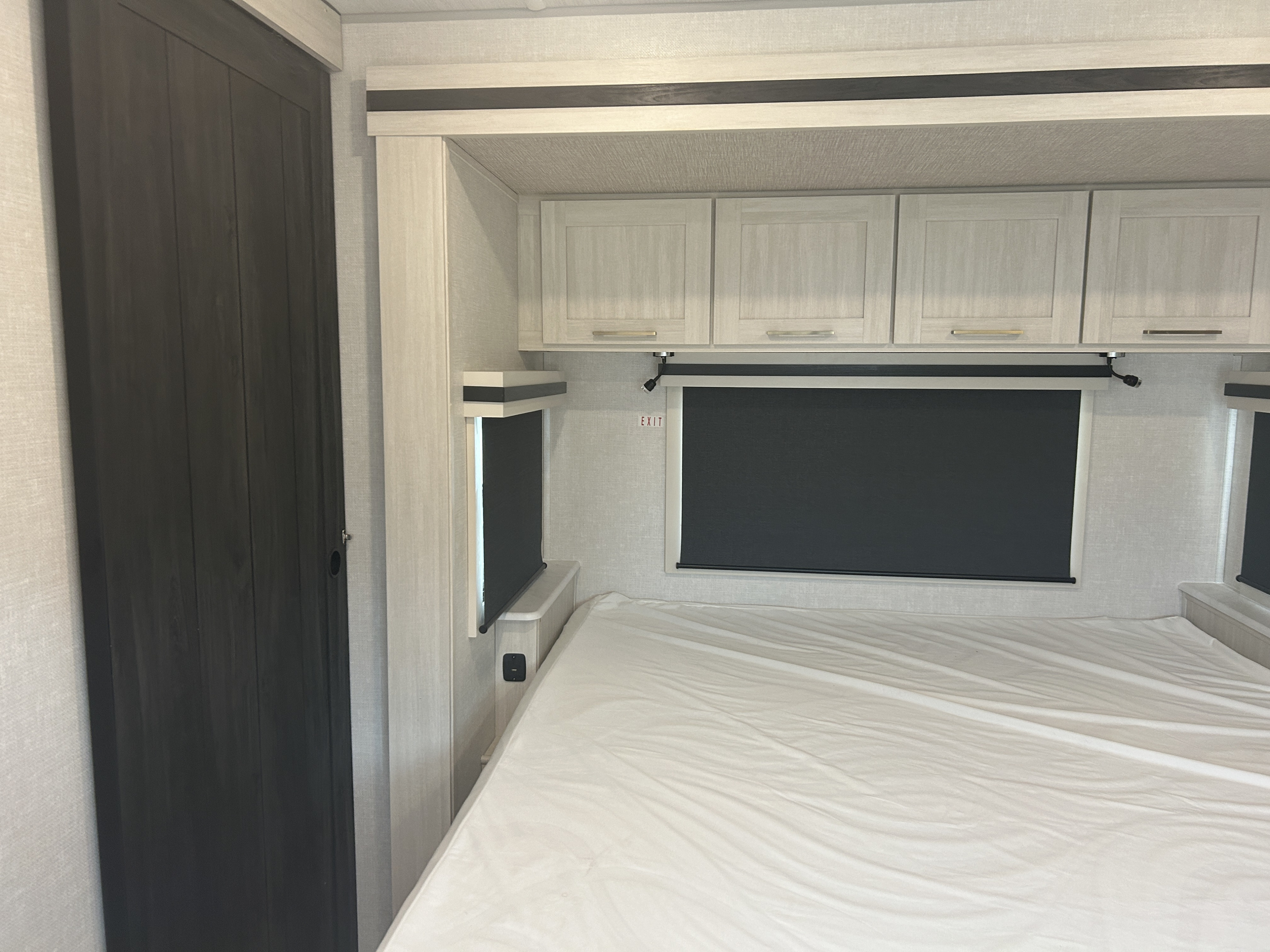 Clean RV rental bedroom with a white bed, light wood cabinets, dark blinds, and a contrasting sliding door.. Forest River Grand Surveyor 2025