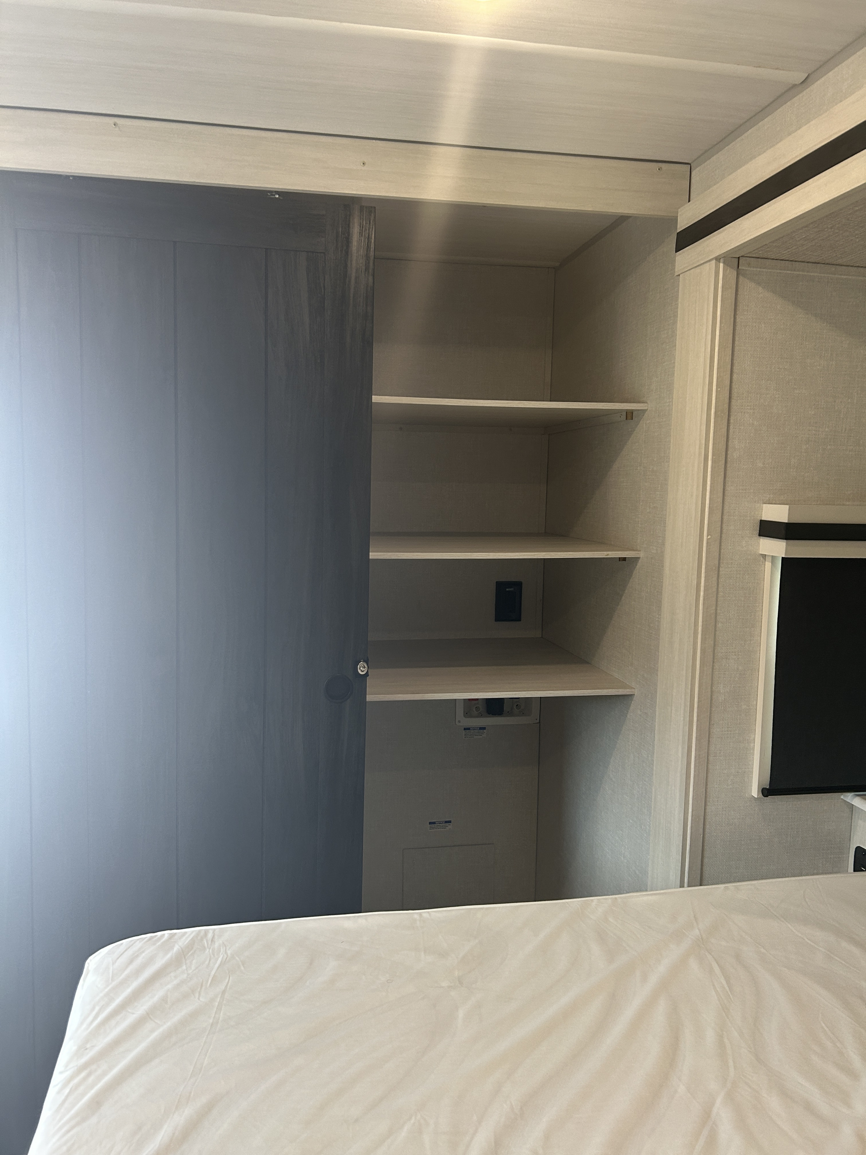 RV rental bedroom: dark sliding closet door, light shelves, utility hookups below, and a bed.. Forest River Grand Surveyor 2025