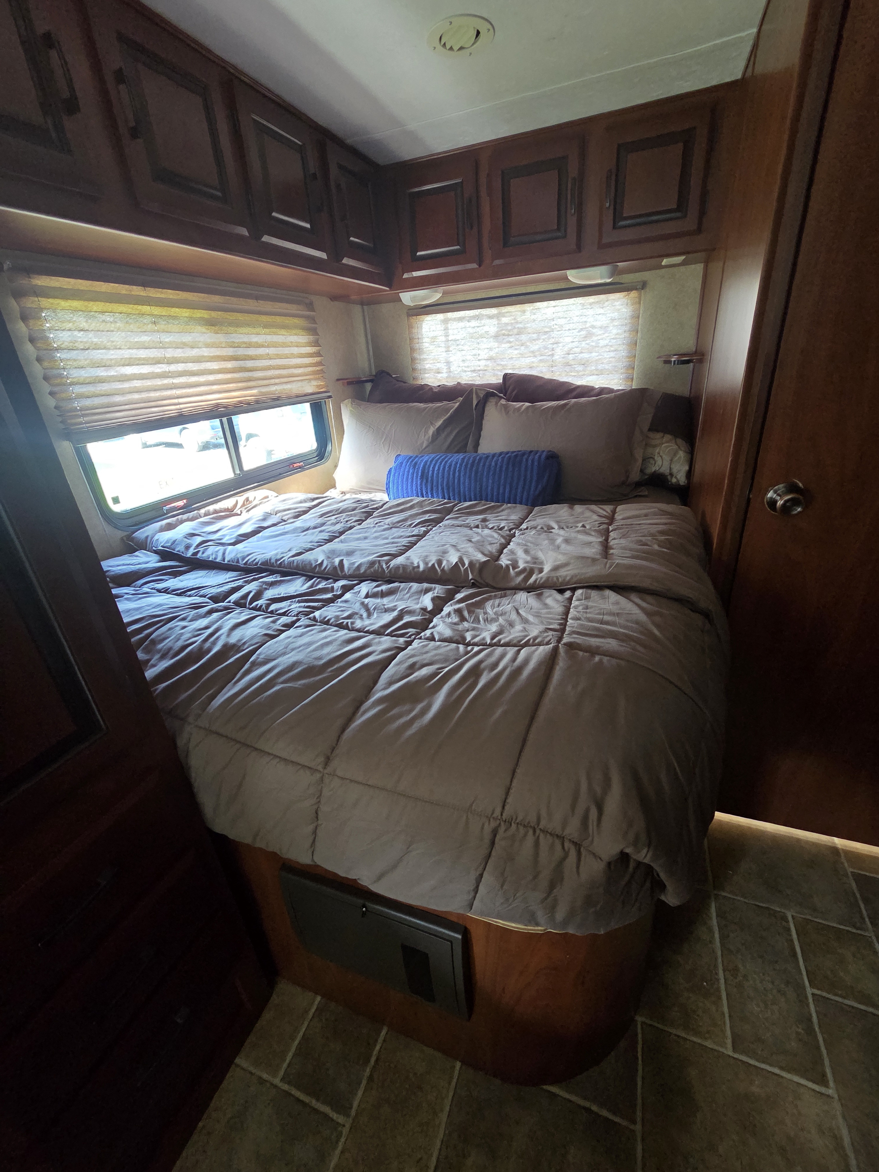 Inviting RV rental bedroom features a comfy bed with pillows, windows with blinds, and rich wood overhead cabinets.. Forest River Sunseeker 2012