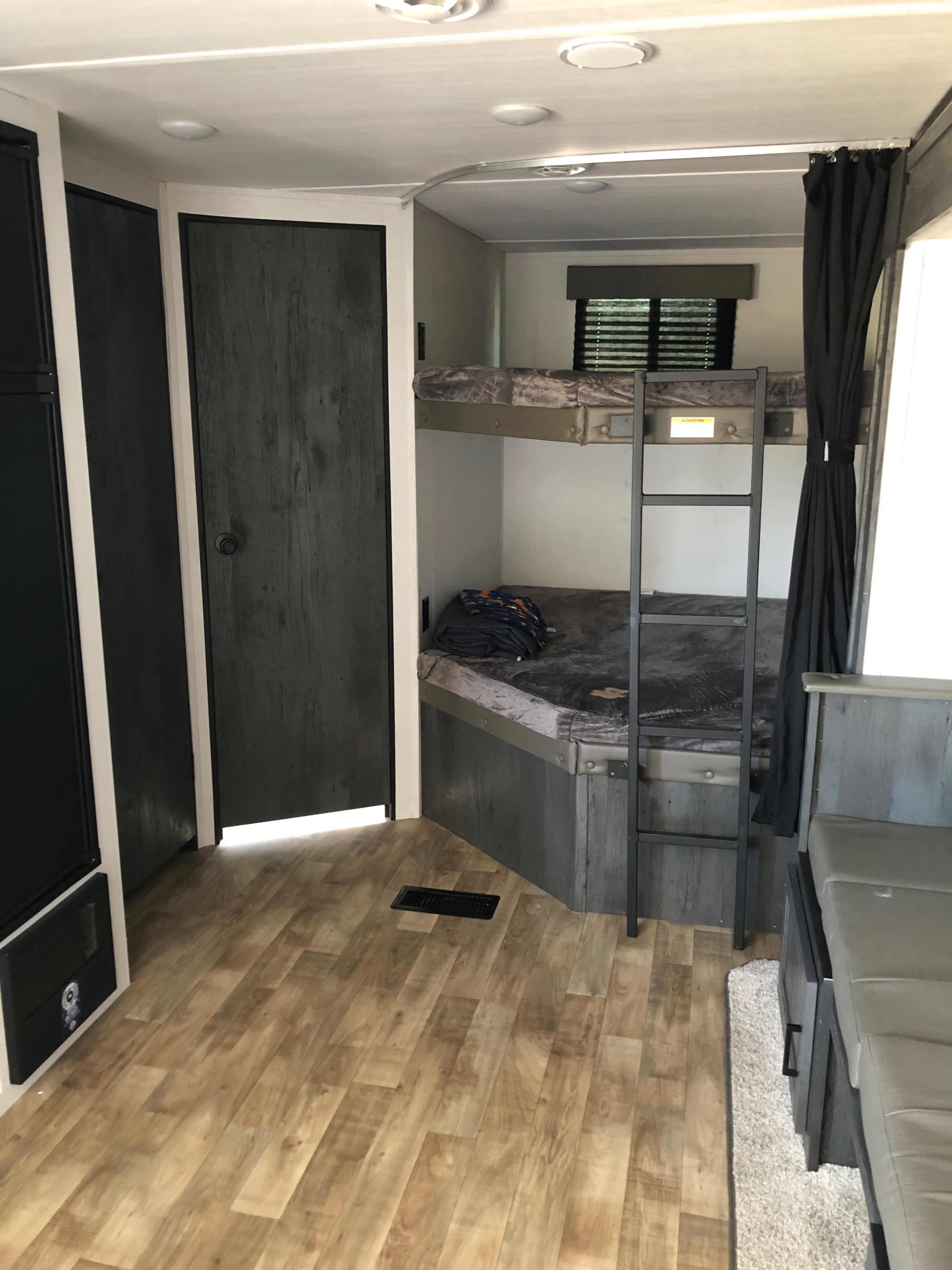 RV rental interior with bunk beds, dark door, and wood-look flooring, showing efficient use of space in this camper.. Keystone RV Hideout 2023