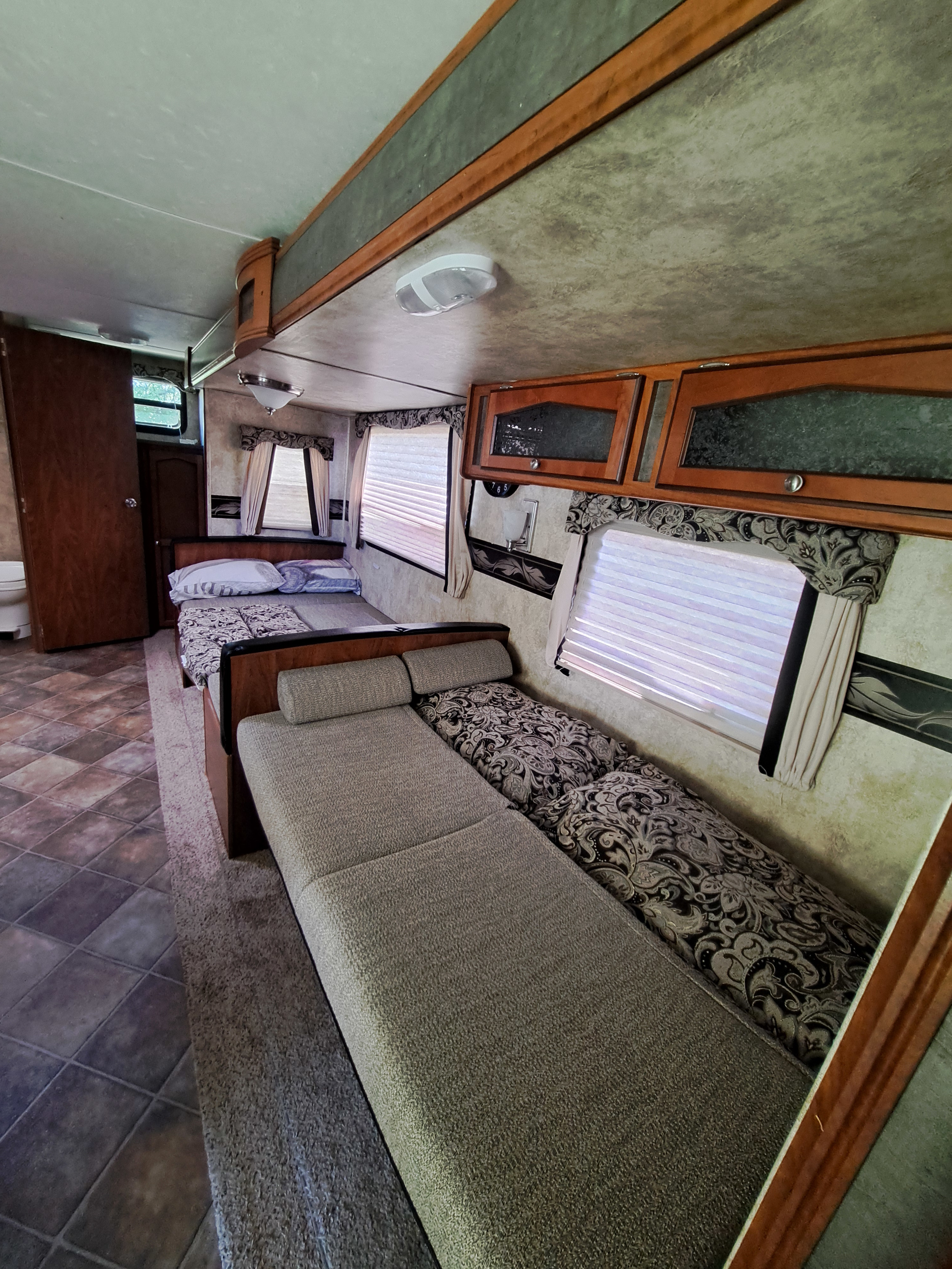 This RV rental interior shows a cozy living/sleeping area with multiple beds, overhead cabinets, and windows with blinds.. Keystone RV Passport Ultra Lite 2012