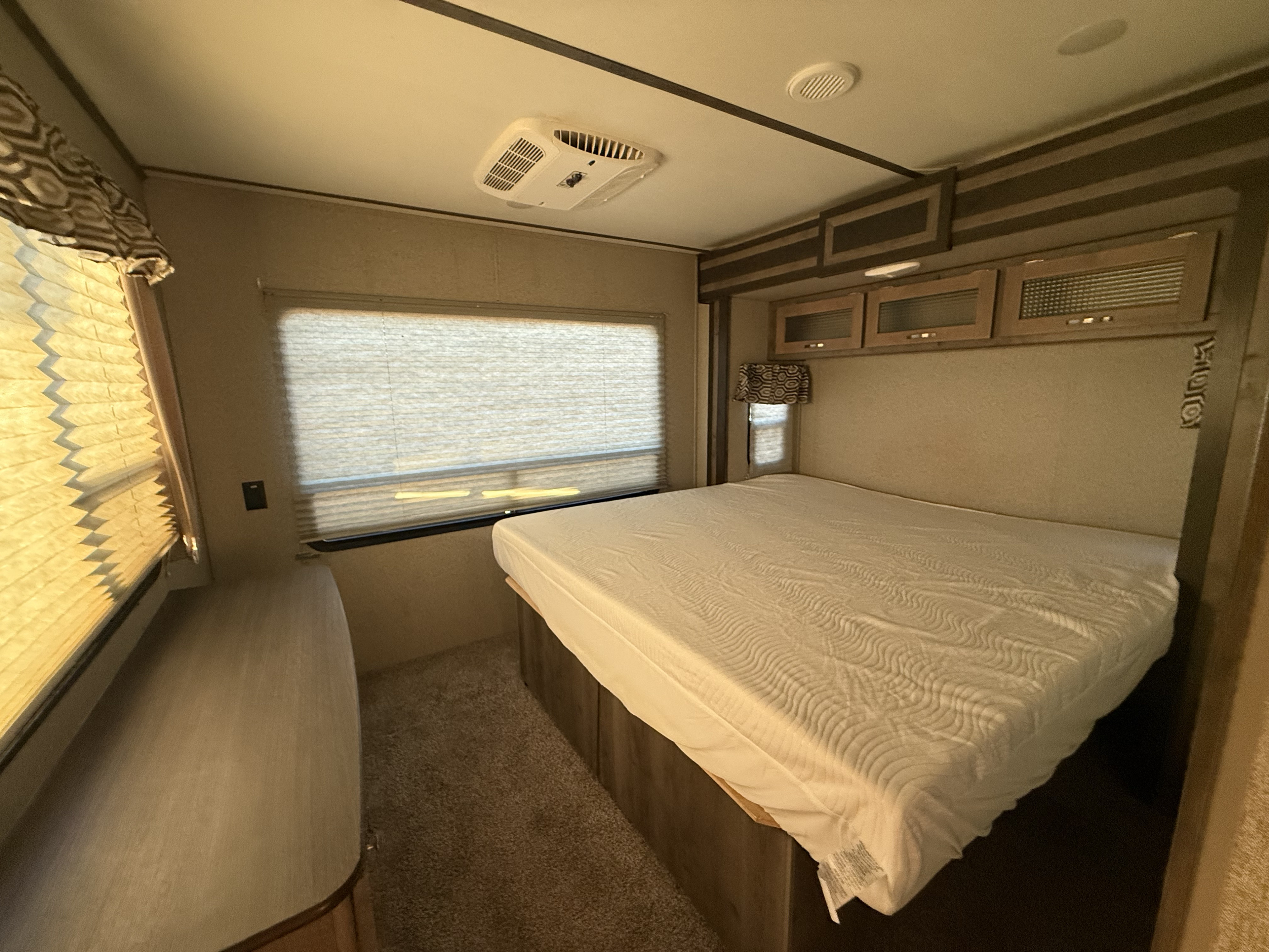 RV rental bedroom with a white mattress, overhead cabinets, window blinds, and a ceiling-mounted AC unit.. Keystone RV Sprinter 2019