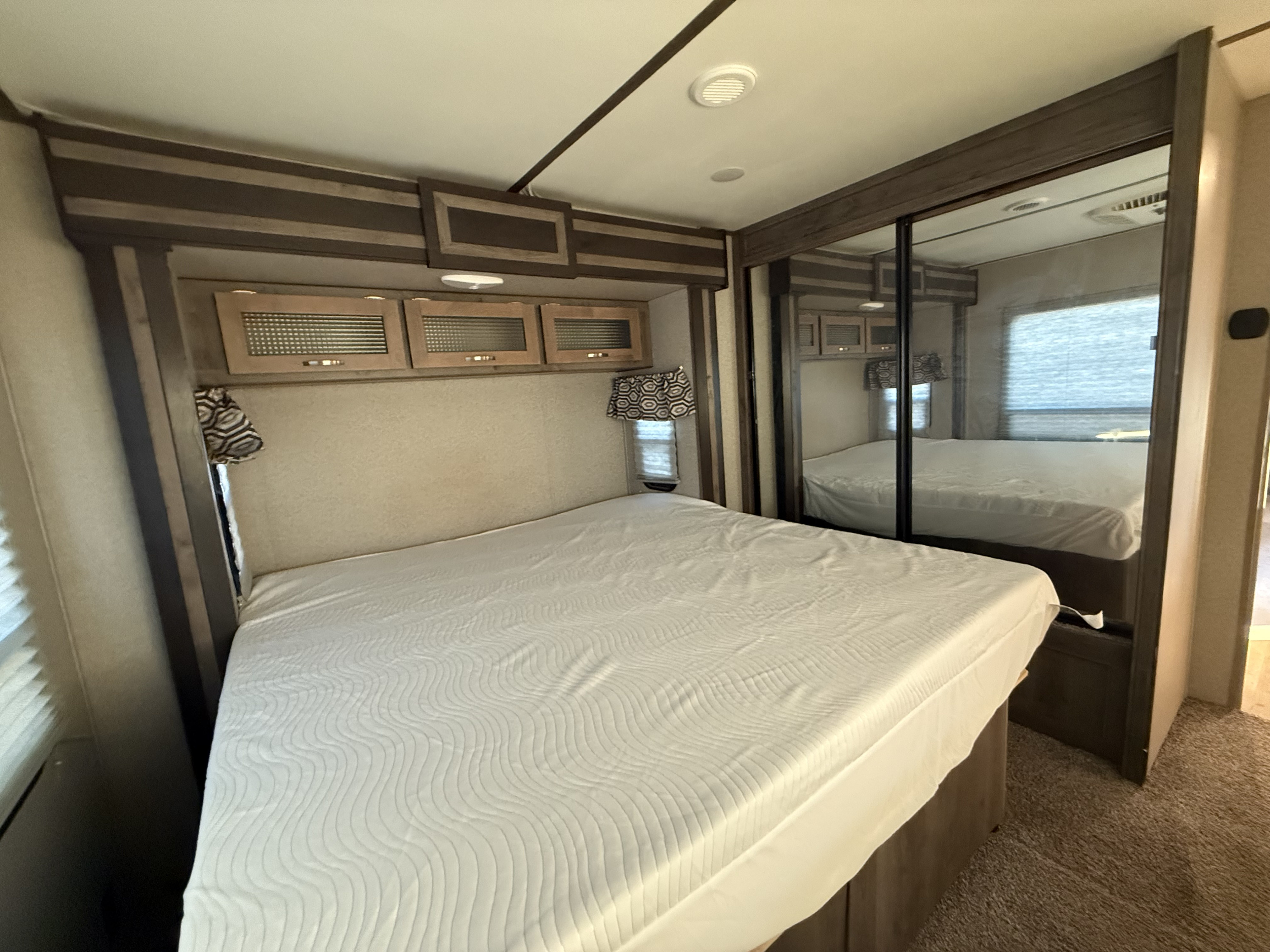 Modern RV rental bedroom features a queen bed, ample storage in overhead cabinets, and a mirrored wardrobe for convenience.. Keystone RV Sprinter 2019