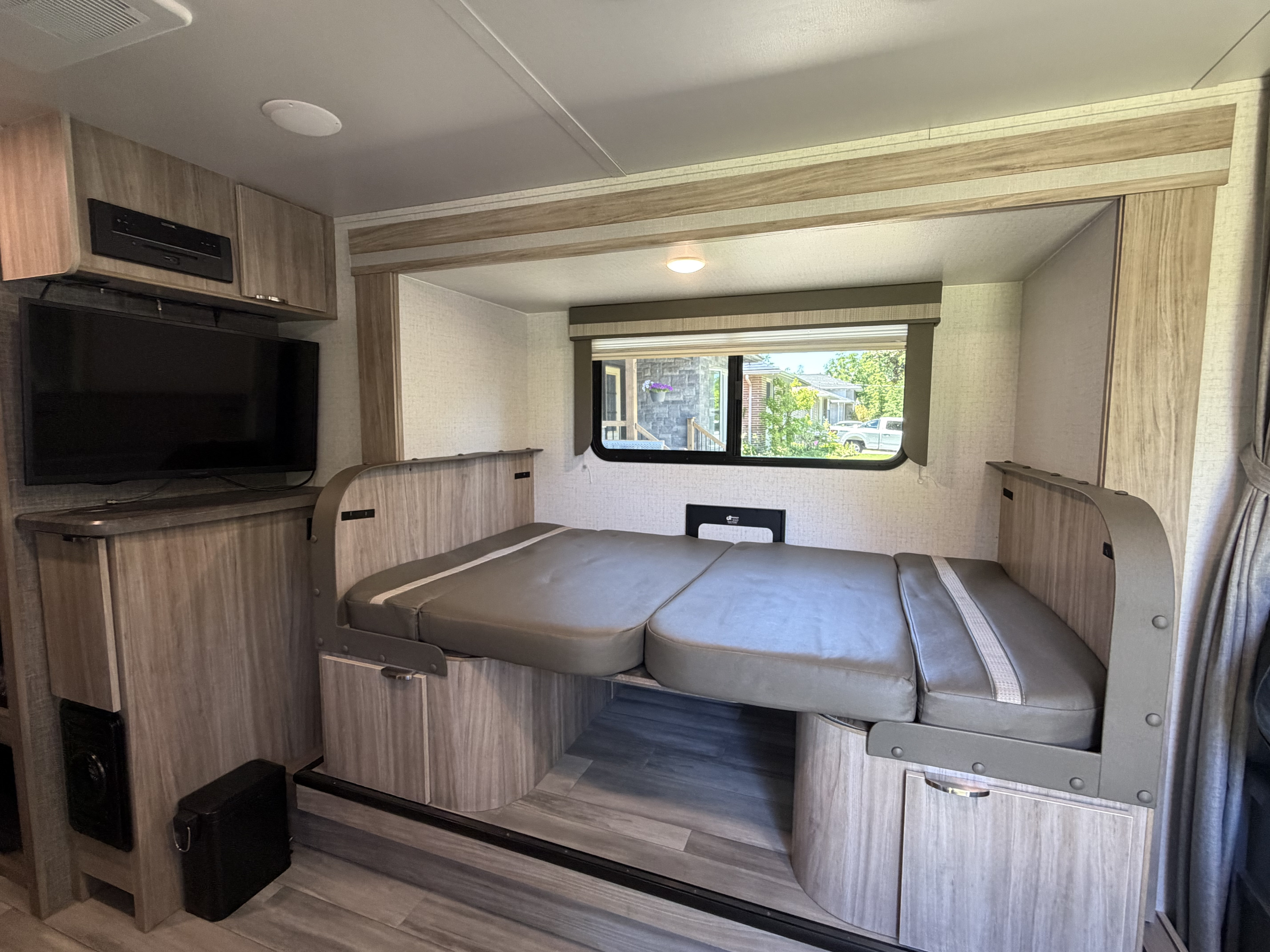 RV rental interior featuring a grey cushioned bed/couch, entertainment center with TV, and a window revealing an outdoor scene.. Minnie Micro Minnie 2021