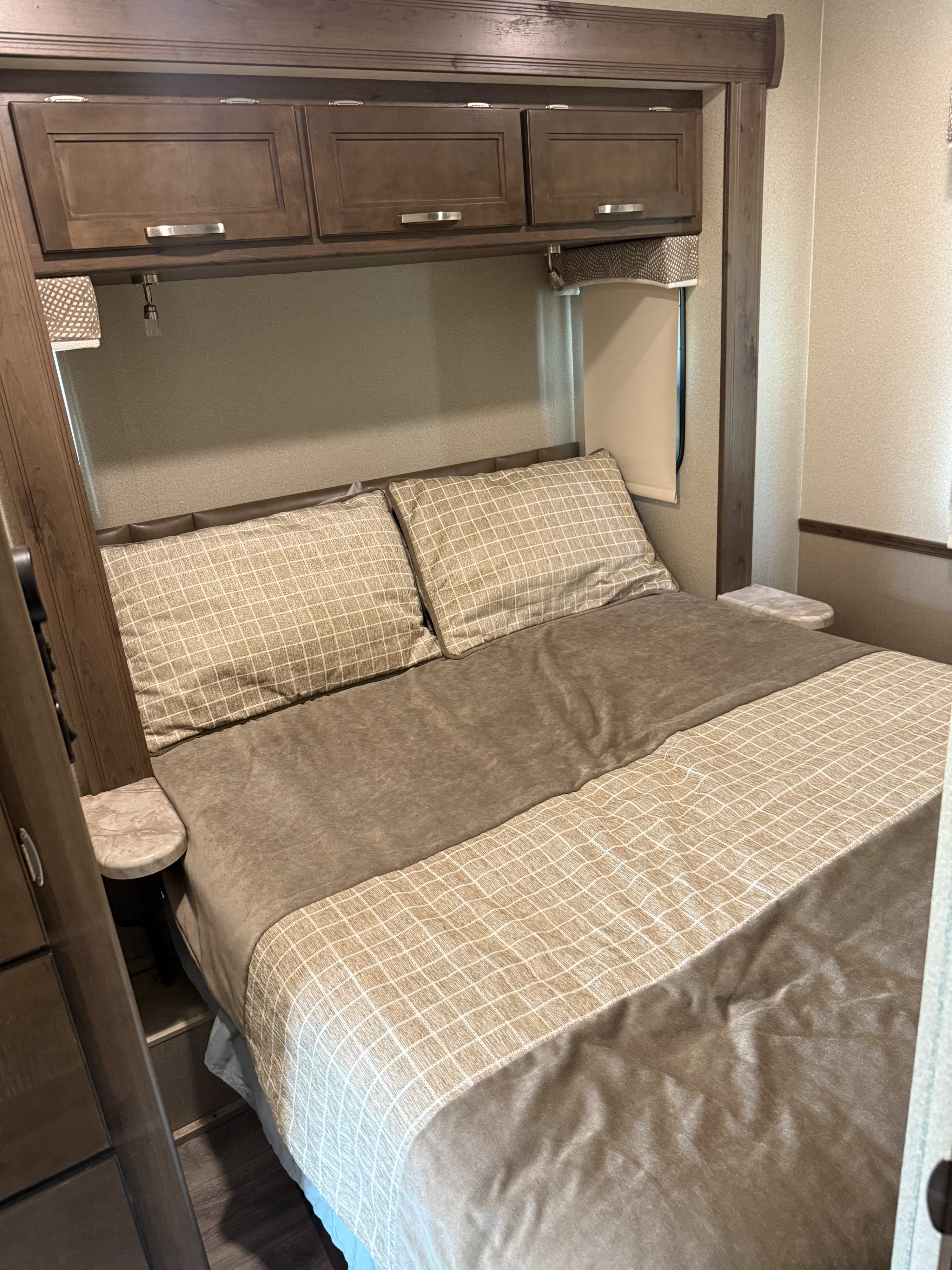 Inside this RV rental: a neat bedroom with grid-patterned bedding, wood cabinets, and small bedside tables.. Entegra Coach Vision 2020