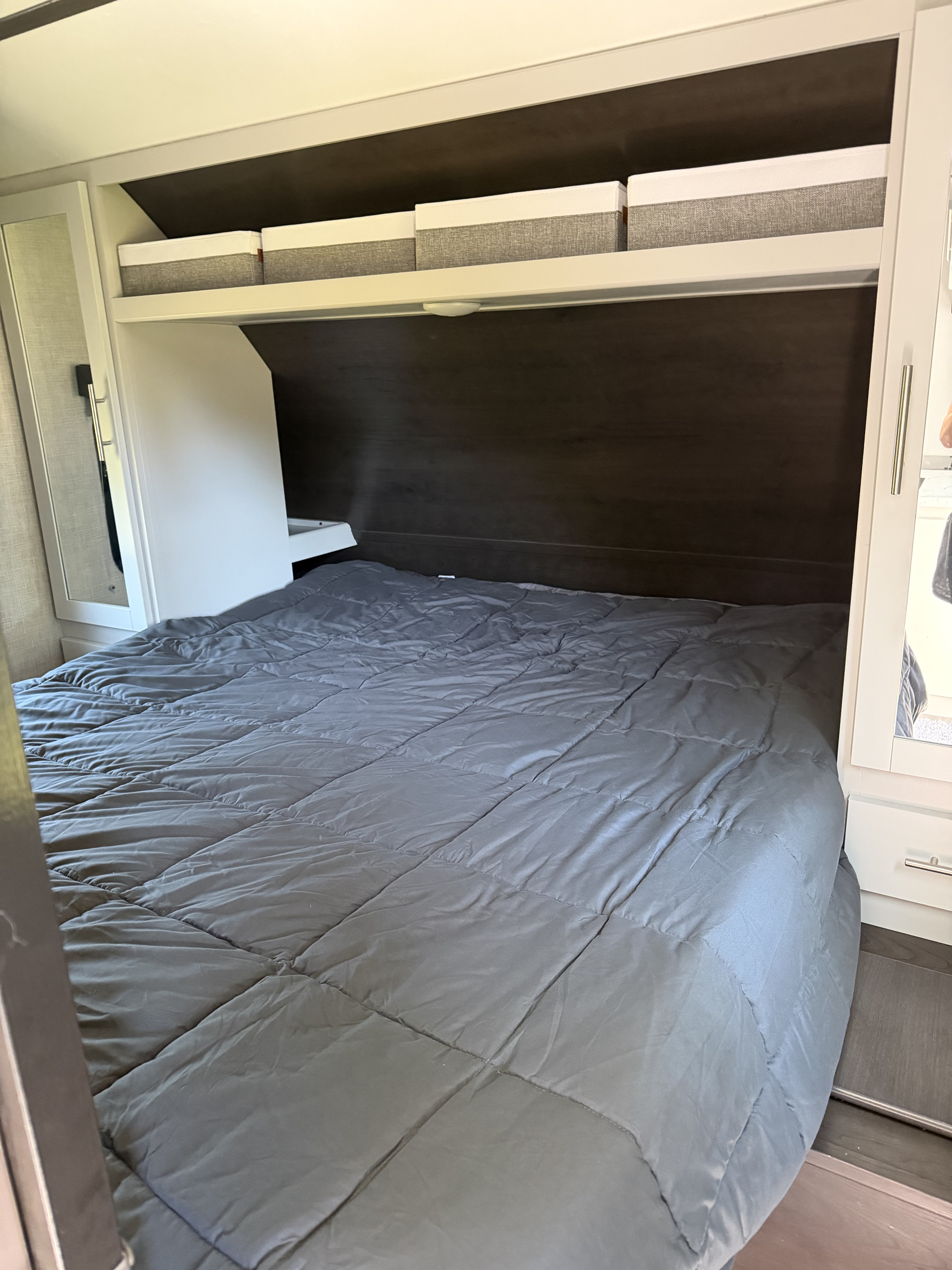 Inside an RV rental: a neat bedroom with a grey comforter, overhead storage boxes, and built-in cabinets.. Keystone RV Bullet Ultra Lite 2021