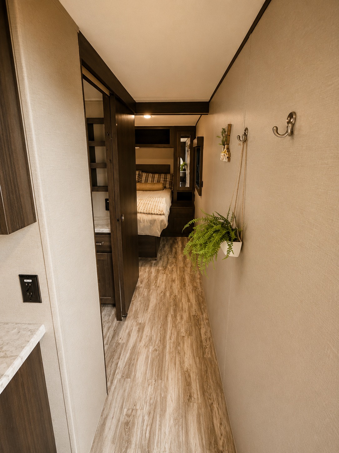 RV rental interior: A well-lit hallway with wood-look flooring leads to a compact bedroom, featuring a plant, hooks, and sliding door.. Grand Design Other 2022