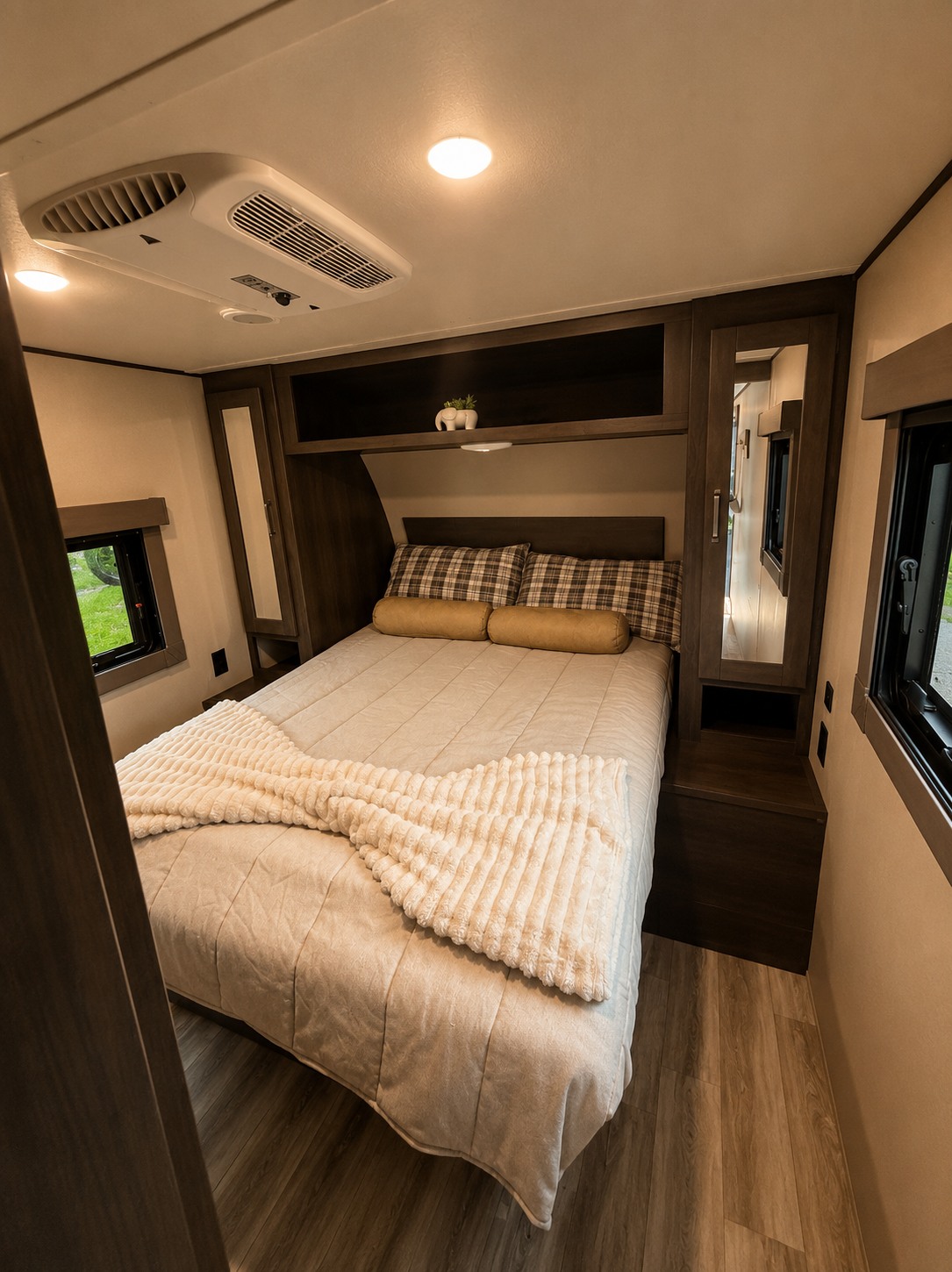 Experience comfort in this modern RV rental bedroom featuring a plush bed with plaid pillows, overhead storage, and windows.. Grand Design Other 2022