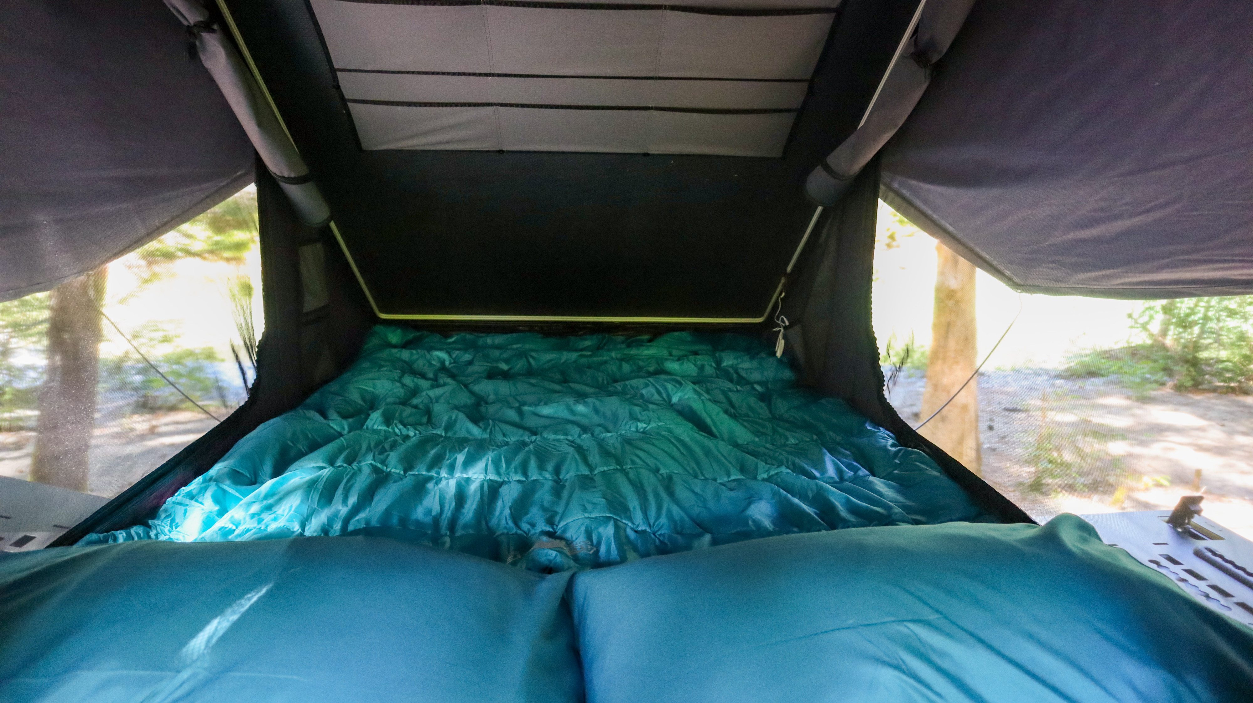 Inside a comfy RV rental's pop-top, a teal bed with pillows and an outdoor view awaits your camping trip.. Toyota Tacoma 2025