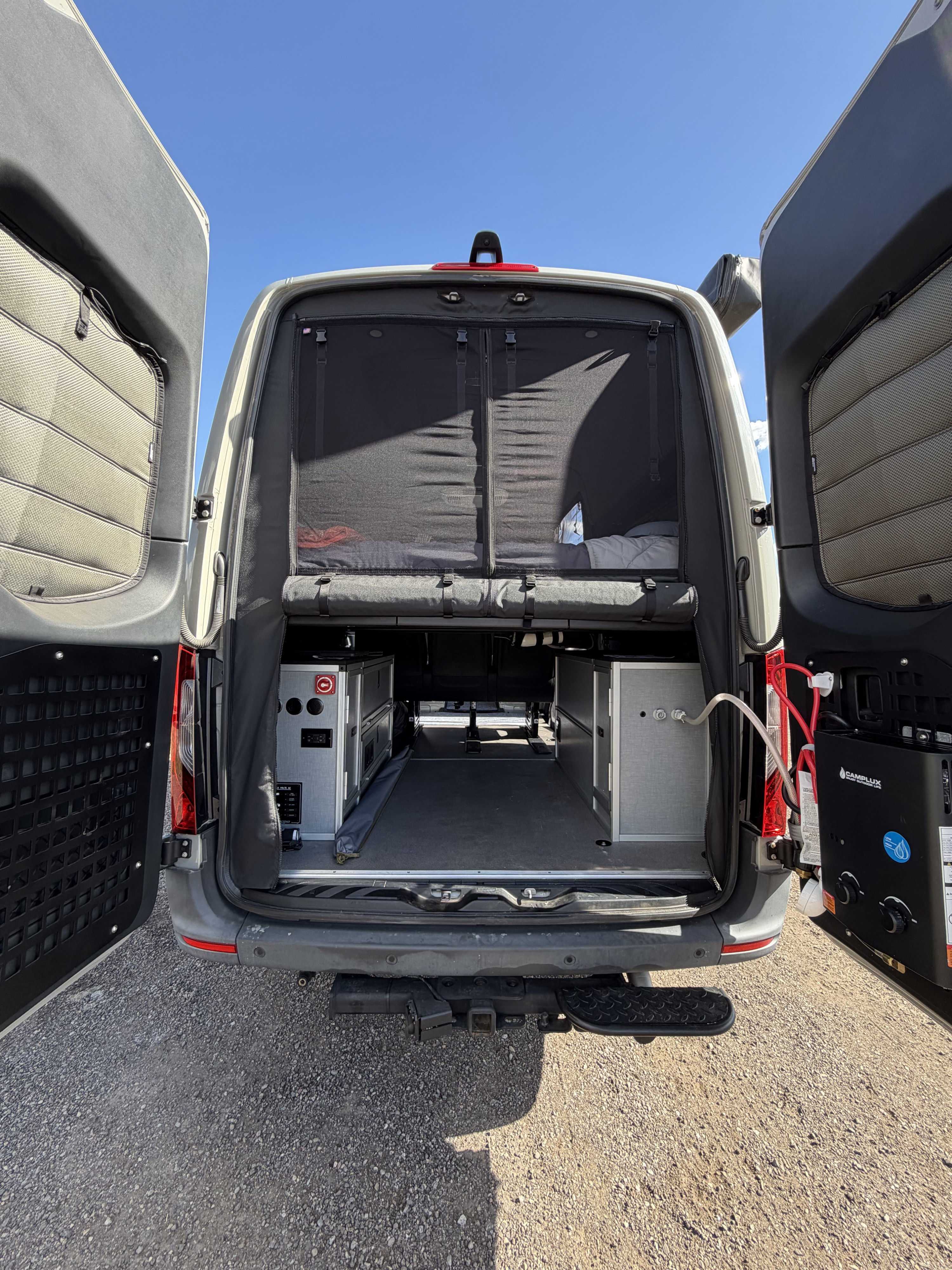 An RV rental's open rear doors expose organized interior storage, a bed, & an outdoor water heater on the right.. Mercedes-Benz Sprinter 2022