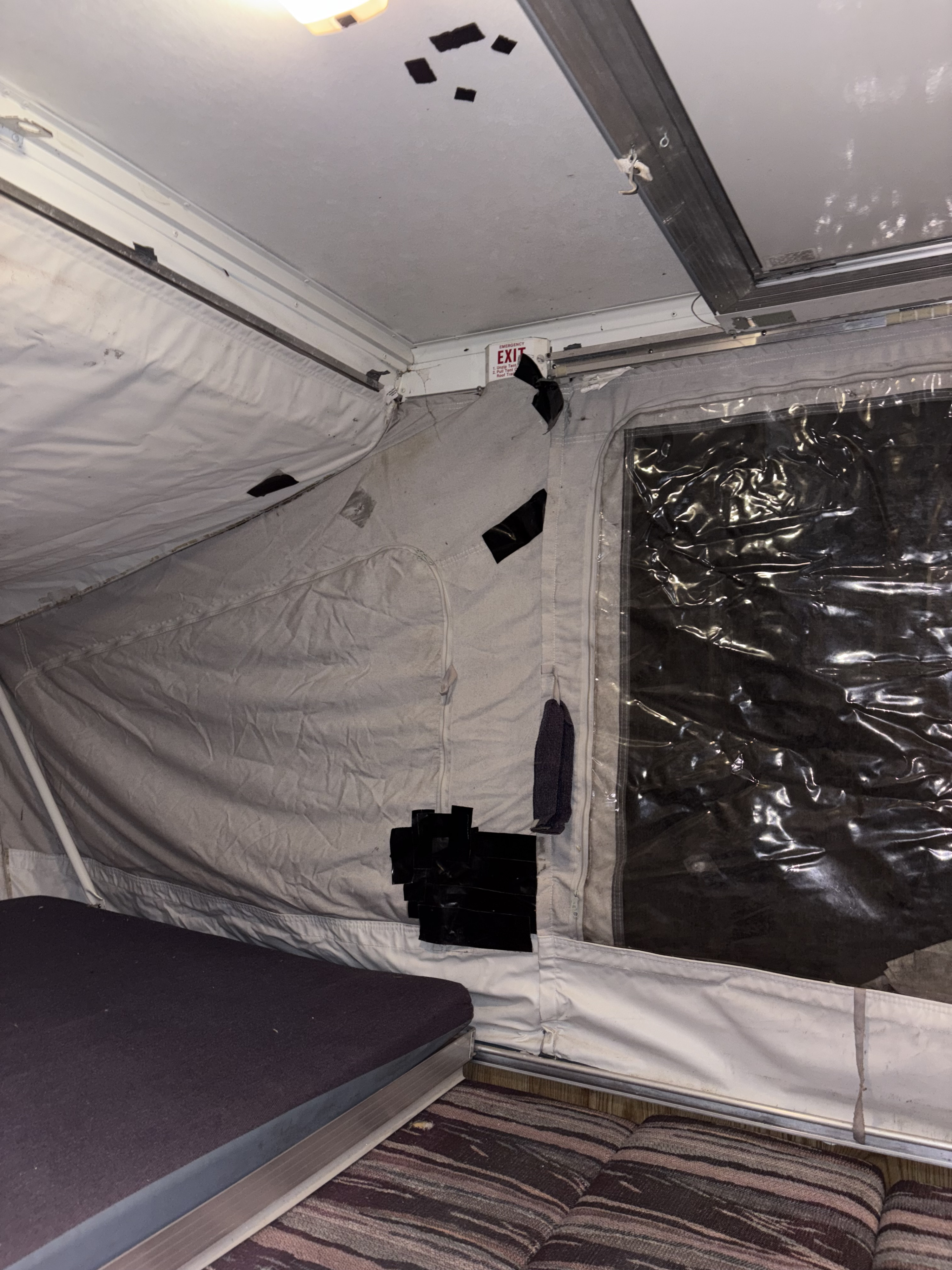 RV rental pop-up camper interior: canvas walls with tape repairs, clear window, bed, and emergency exit.. Fleetwood Coleman Rio Grande 1995