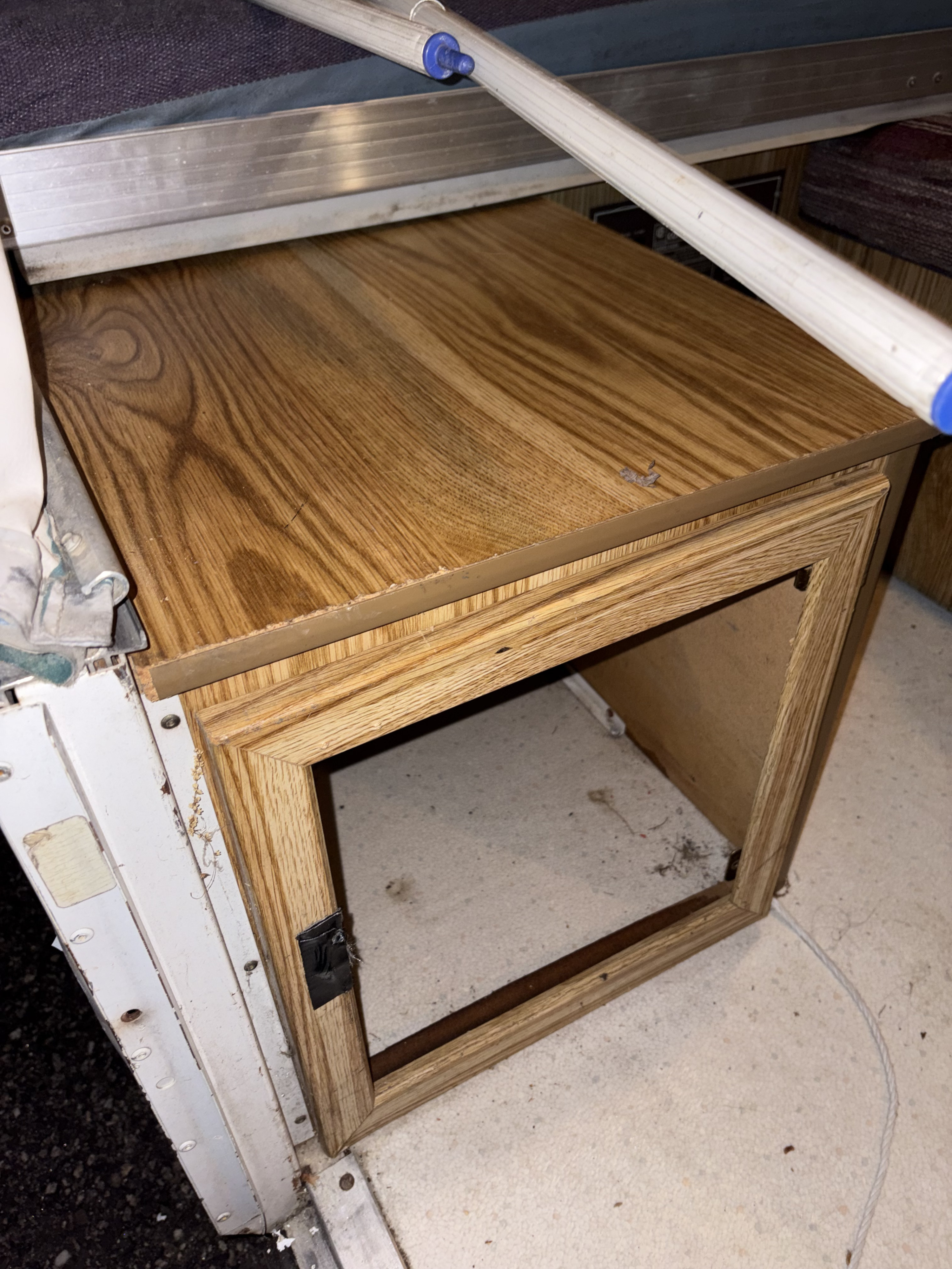 RV rental space: a small, open wood-look cabinet, with part of a bed frame above and textured floor.. Fleetwood Coleman Rio Grande 1995