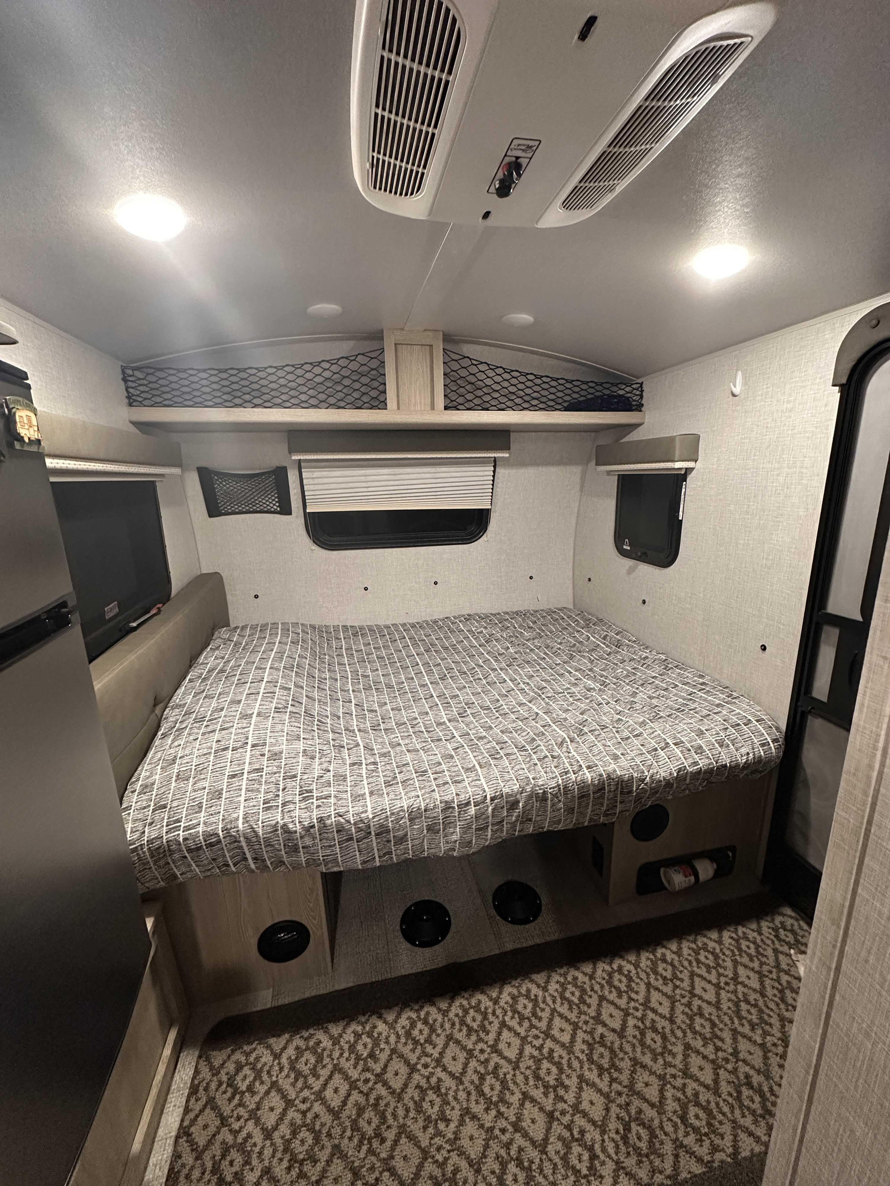 Cozy RV rental bedroom featuring a large bed, overhead storage nets, windows, an AC unit, and patterned carpet.. Forest River Rockwood Geo Pro 2021