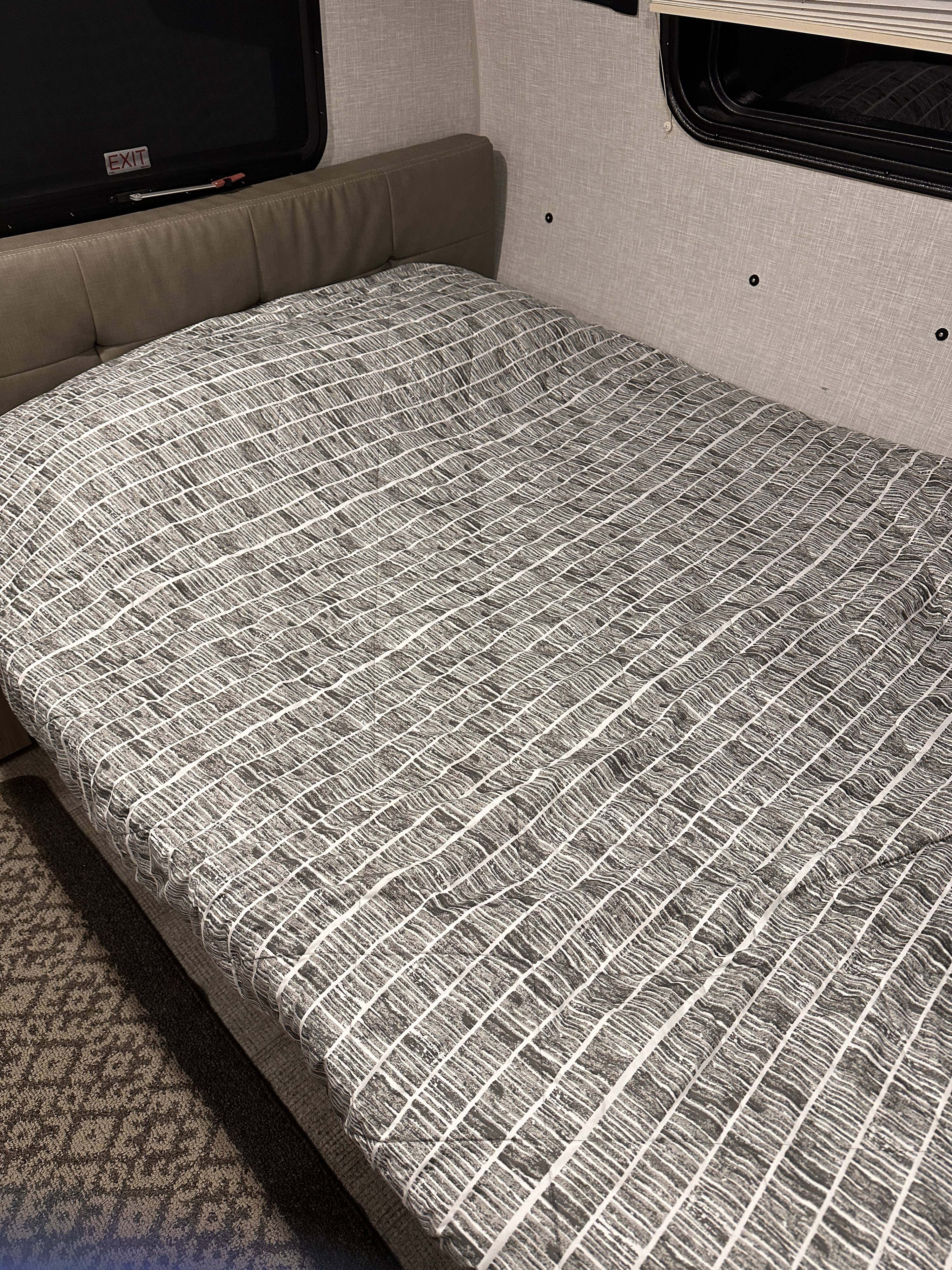 Cozy RV rental interior featuring a neatly made bed with a striped comforter and an emergency exit window.. Forest River Rockwood Geo Pro 2021