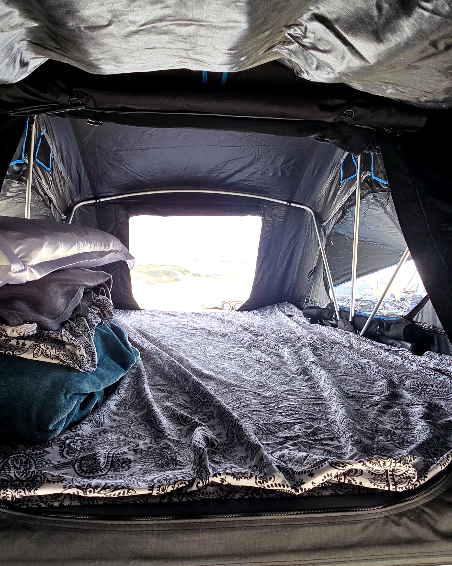 Inside an RV rental rooftop tent: a cozy bed with paisley bedding, pillows, and a bright view of the outdoors.. Beyond Outdoors Roof tent 2026