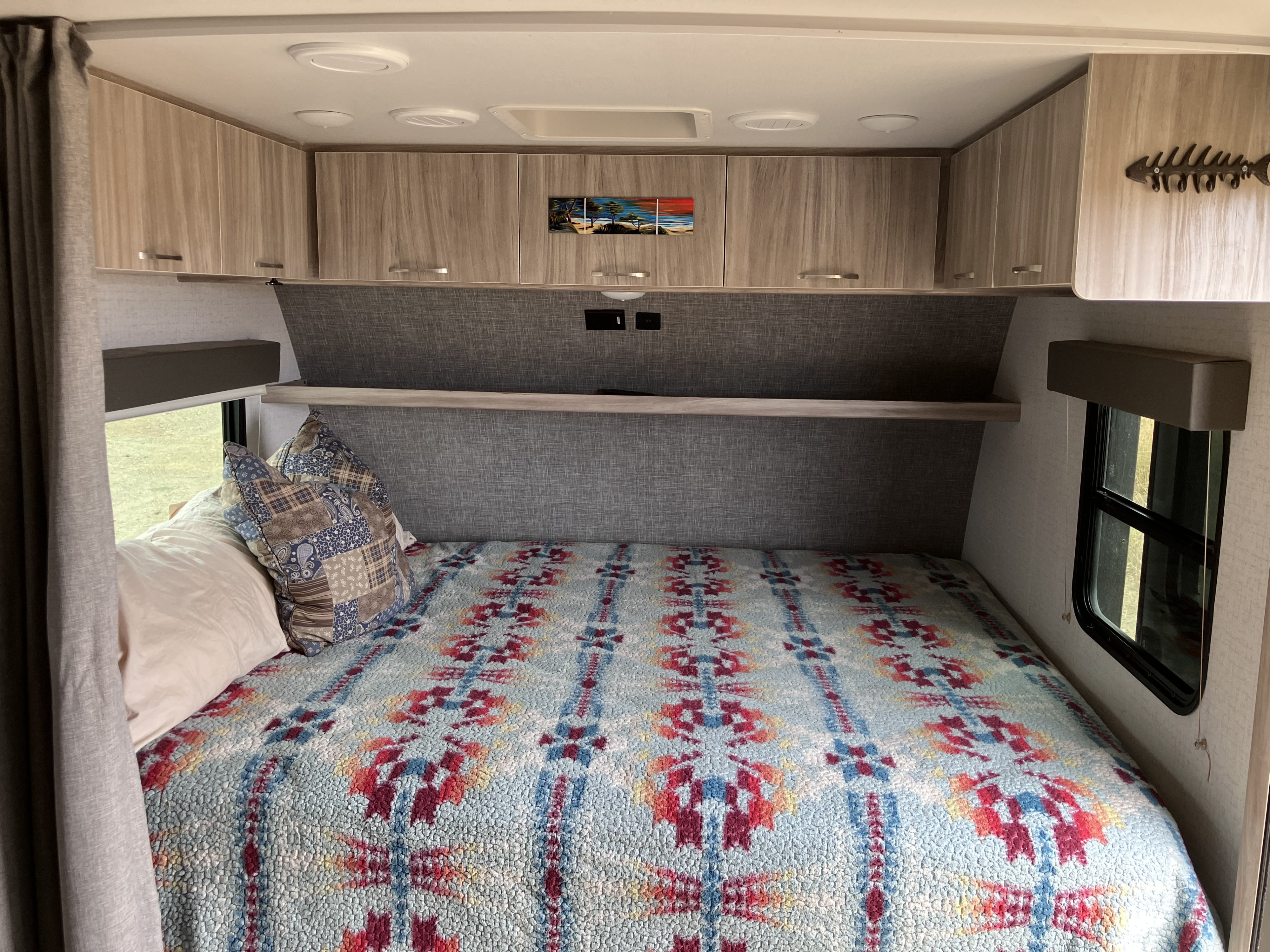 Comfortable RV rental bedroom with a vibrant patterned bedspread, overhead cabinets, and windows for natural light.. Winnebago Micro Winnie 2021
