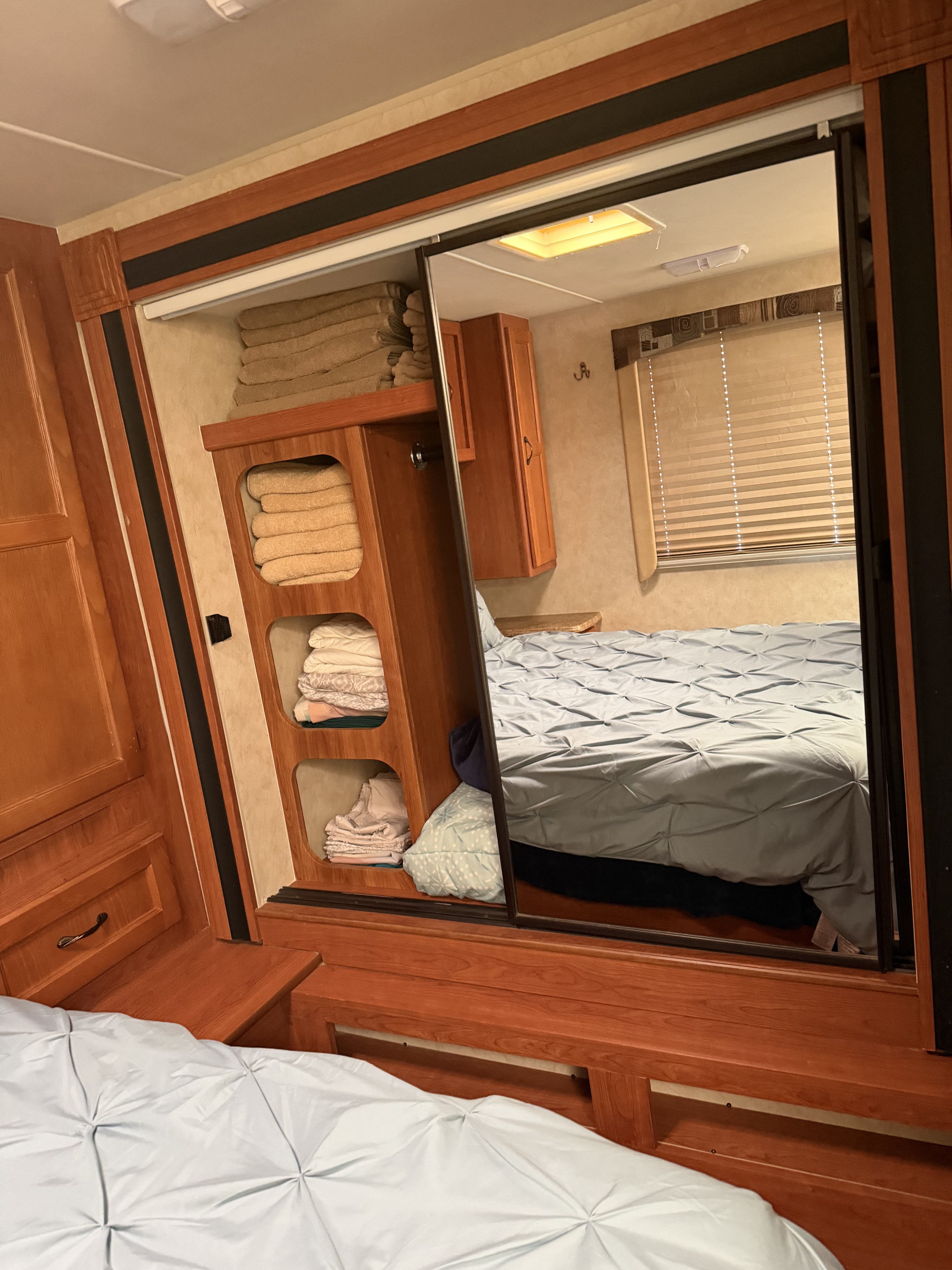 Inside an rv rental: bedroom with light blue bed, wooden storage shelves with towels, and a sliding mirrored closet.. Forest River,Inc Coachman Freelander 2012
