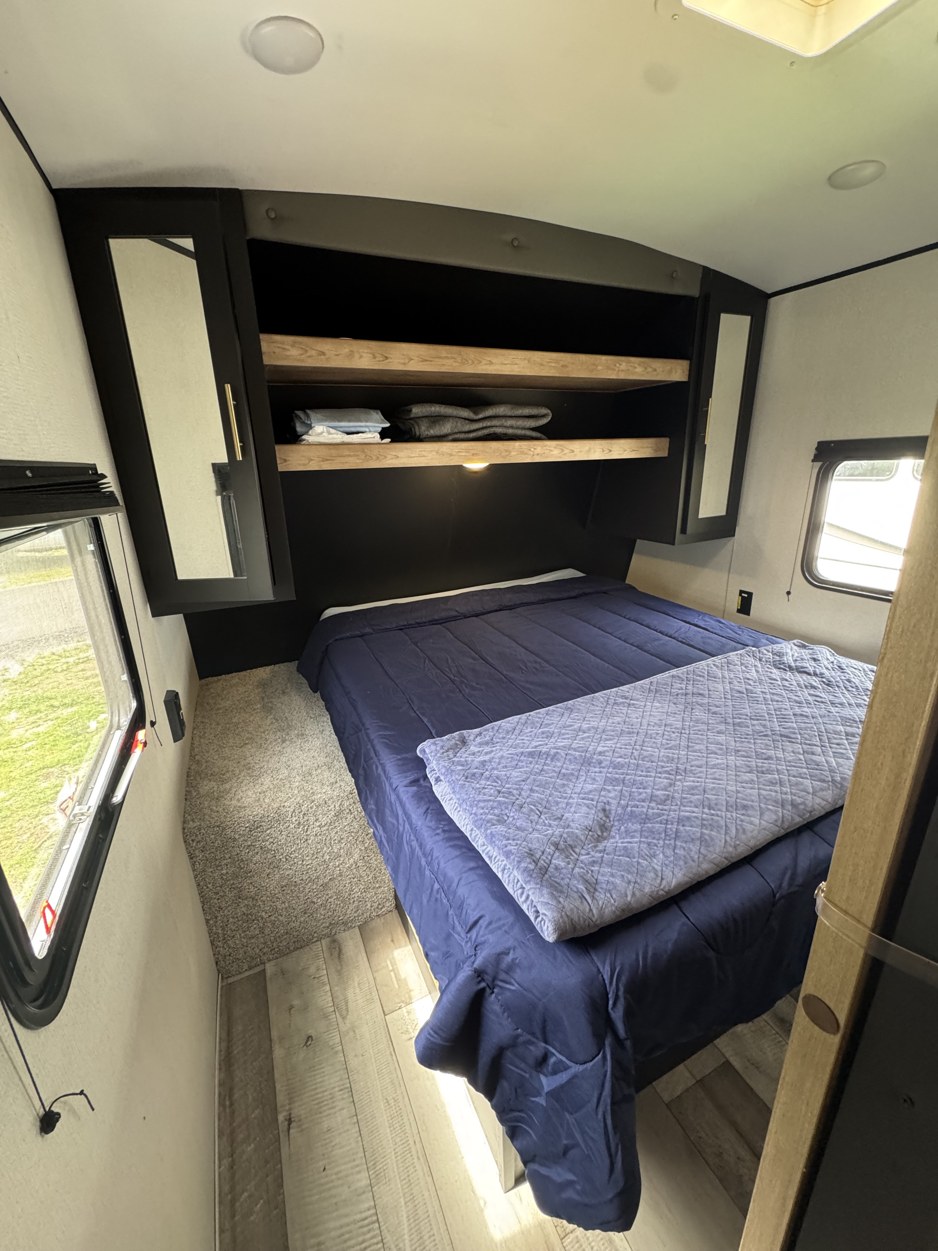 Inside an RV rental bedroom: a bed with blue bedding, overhead shelves, mirrored cabinets, and windows for natural light.. Keystone RV Springdale 2022