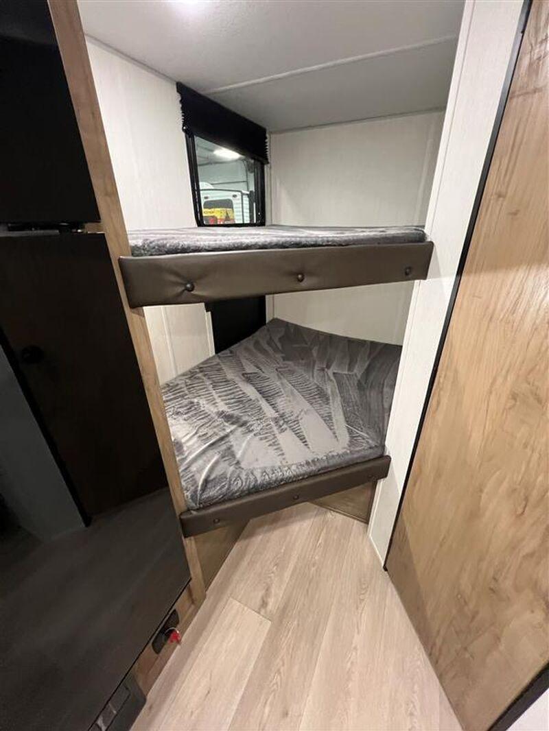 RV rental interior with two compact bunk beds, featuring covered mattresses, a window above the top bunk, and light wood flooring.. Forest River Wolf Pup 2024