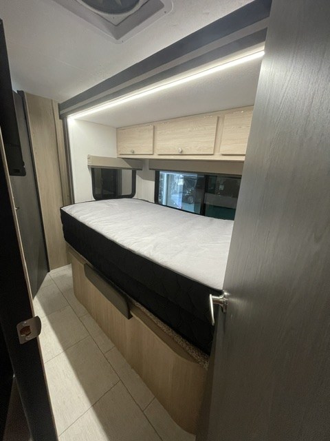 Cozy RV rental sleeping area with a bed, overhead cabinets, and window. Bright LED lighting illuminates the space.. Coachmen LEPRECHAUN 308KB 2027