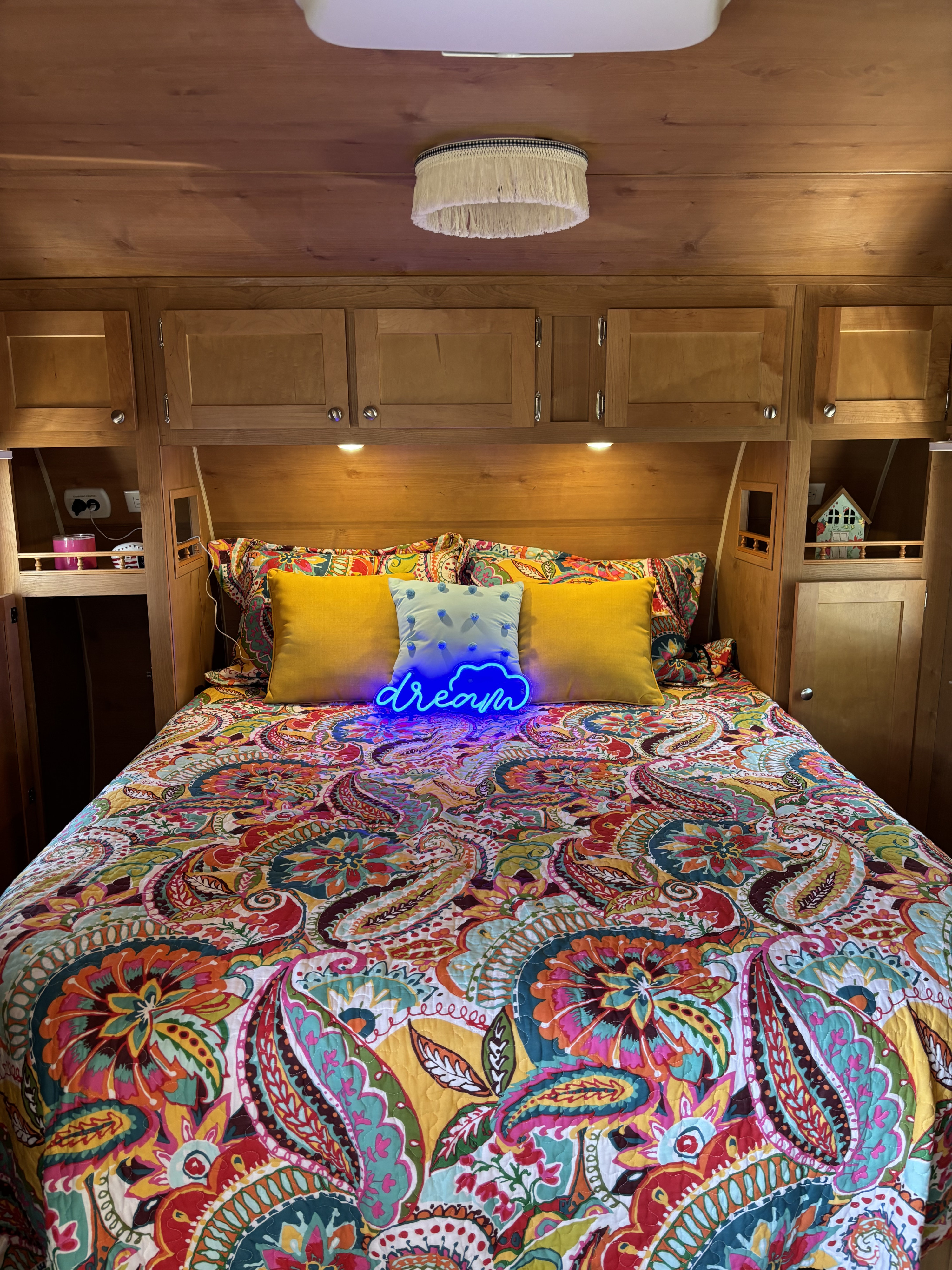 Cozy RV rental bedroom: vibrant paisley bedspread, glowing blue 'dream' sign, and warm wood cabinets.. Riverside Travel Trailer 177 2017