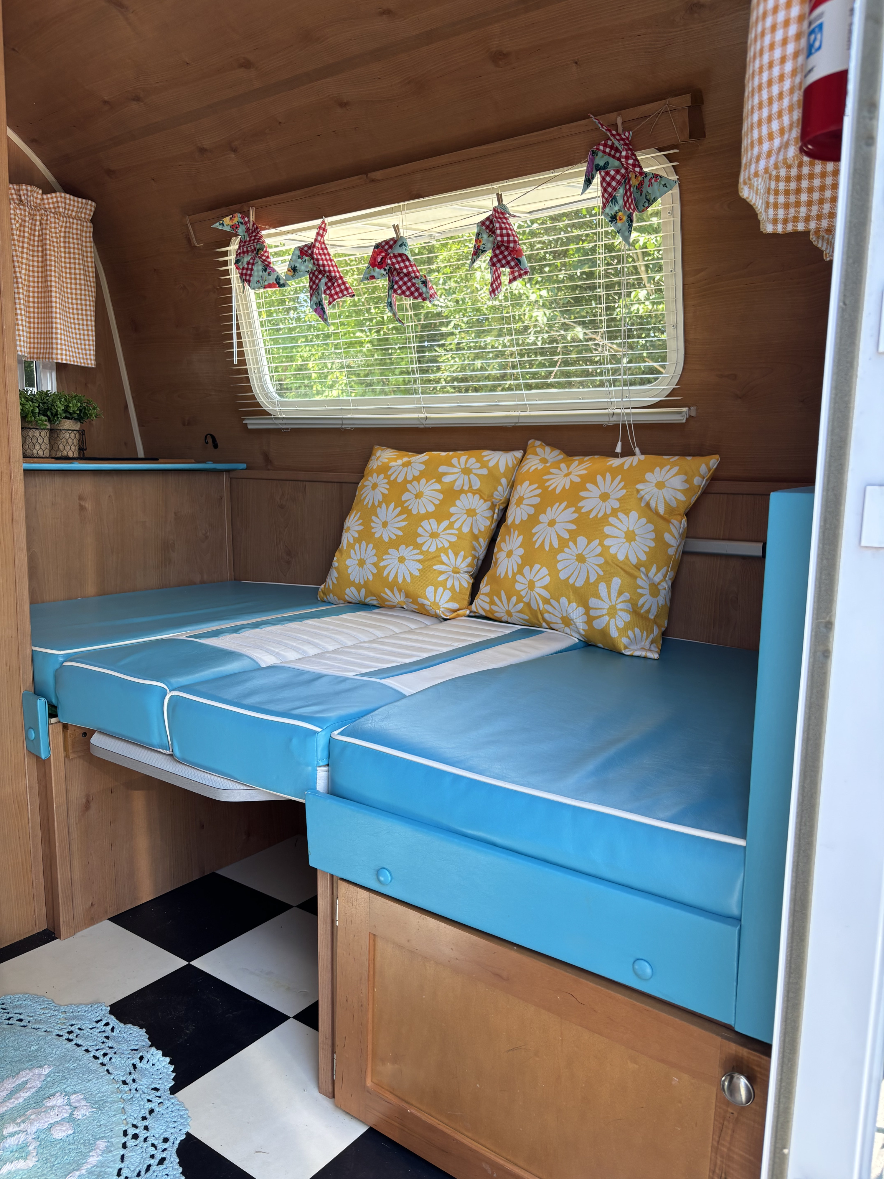 Charming RV rental interior: cozy blue and white bed with sunny daisy pillows, wood paneling, and a classic checkered floor.. Riverside Travel Trailer 177 2017