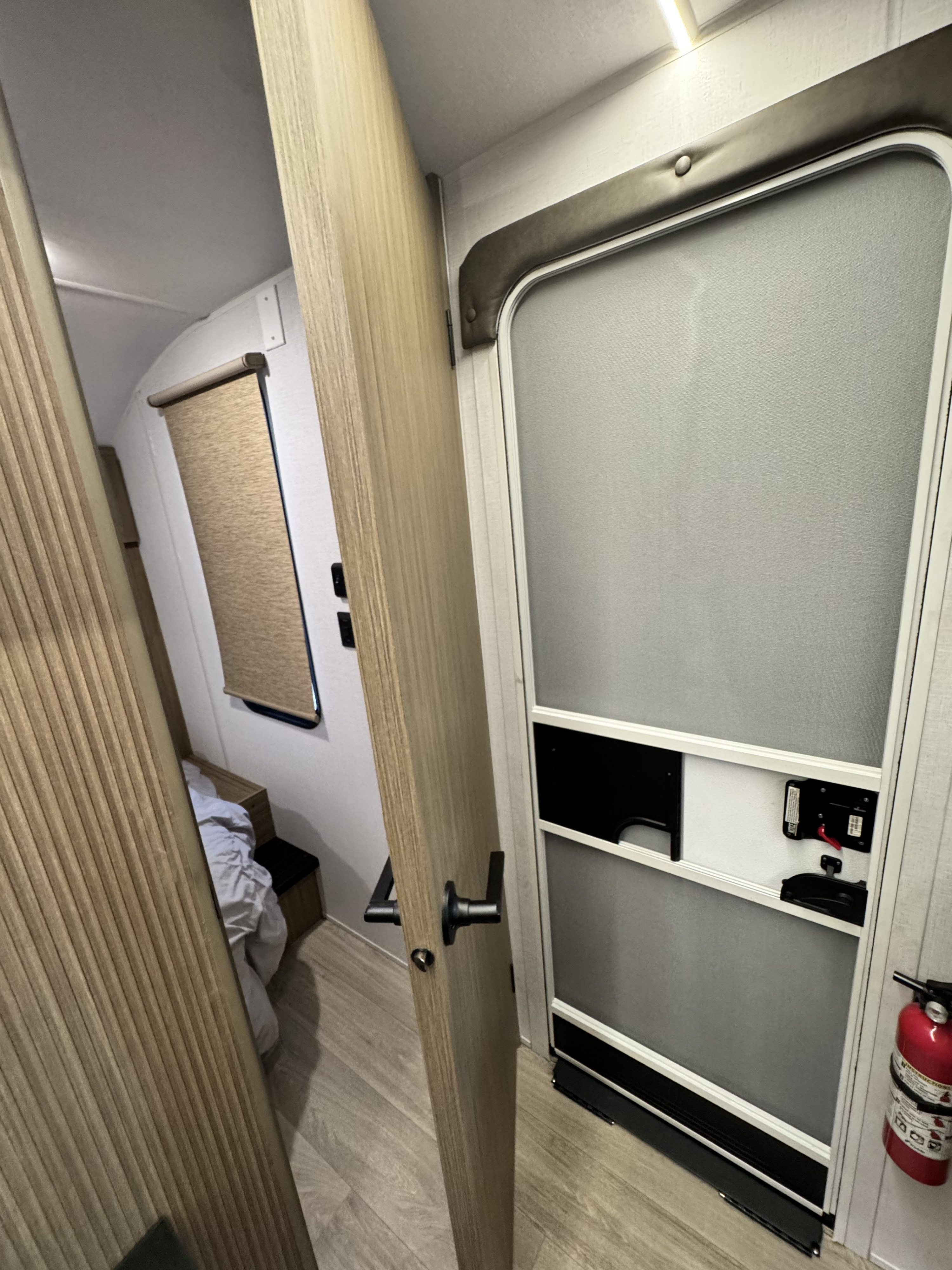 RV rental interior: open wooden door revealing a bed, main entrance with privacy screen, and a red fire extinguisher. Compact space.. Forest River Salem Cruise-Lite 2026