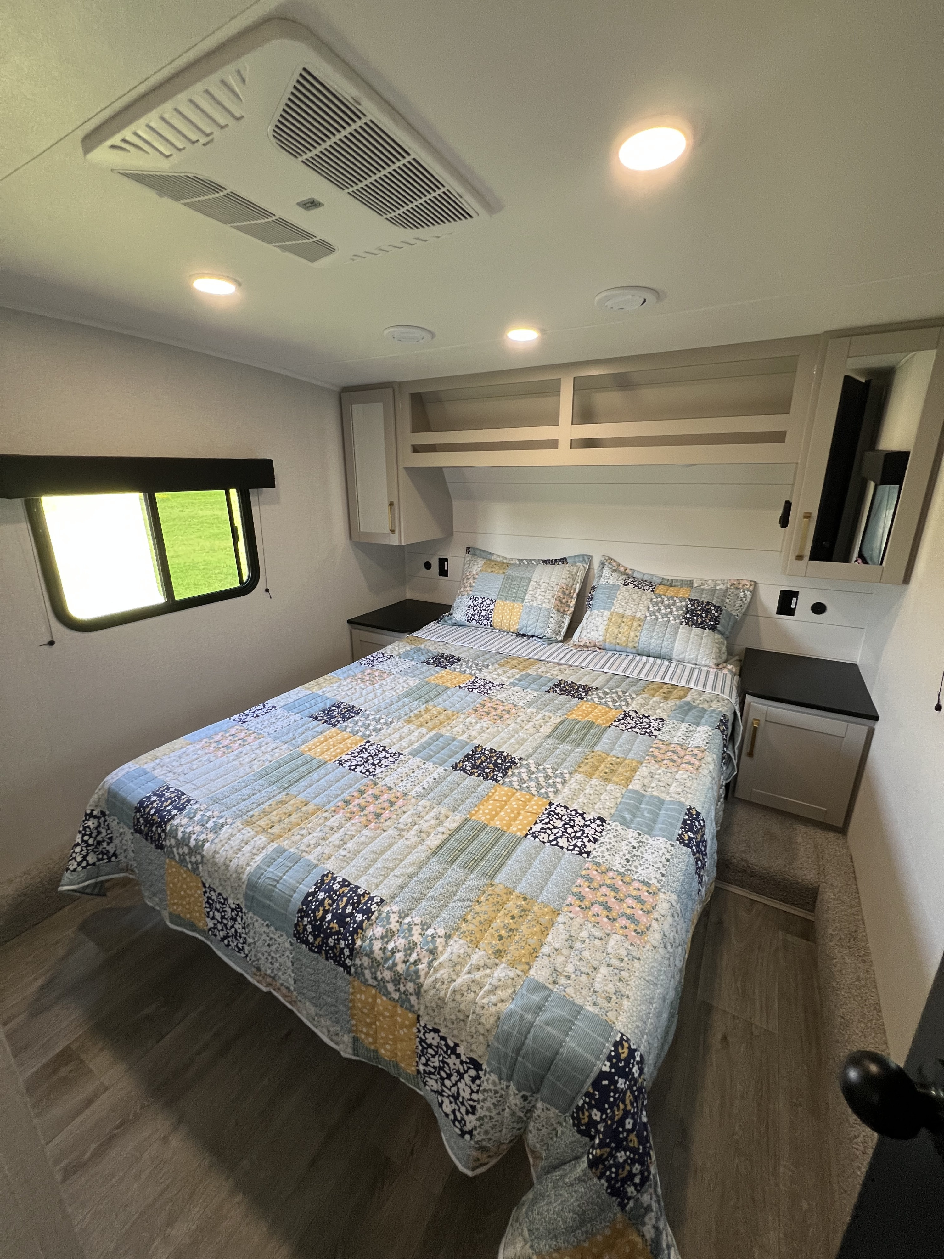 Cozy RV rental bedroom featuring a patchwork quilt, overhead storage, and window views, with AC for comfort.. Sundance xlt 28DB 2026
