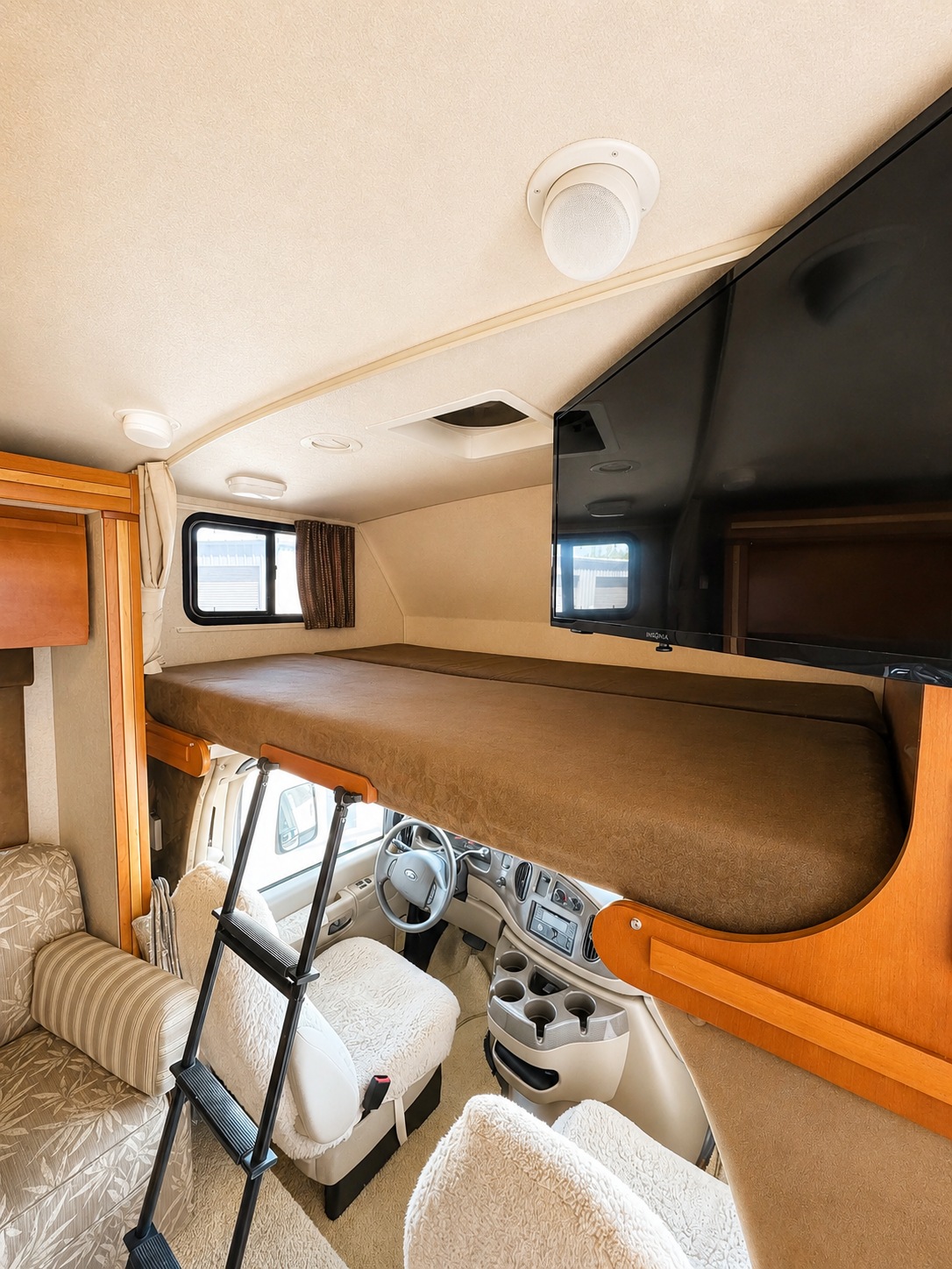 Bright rv rental interior: view of an over-cab bunk bed, driver's cabin below, cozy seating, and mounted TV.. Winnebago Outlook 2008