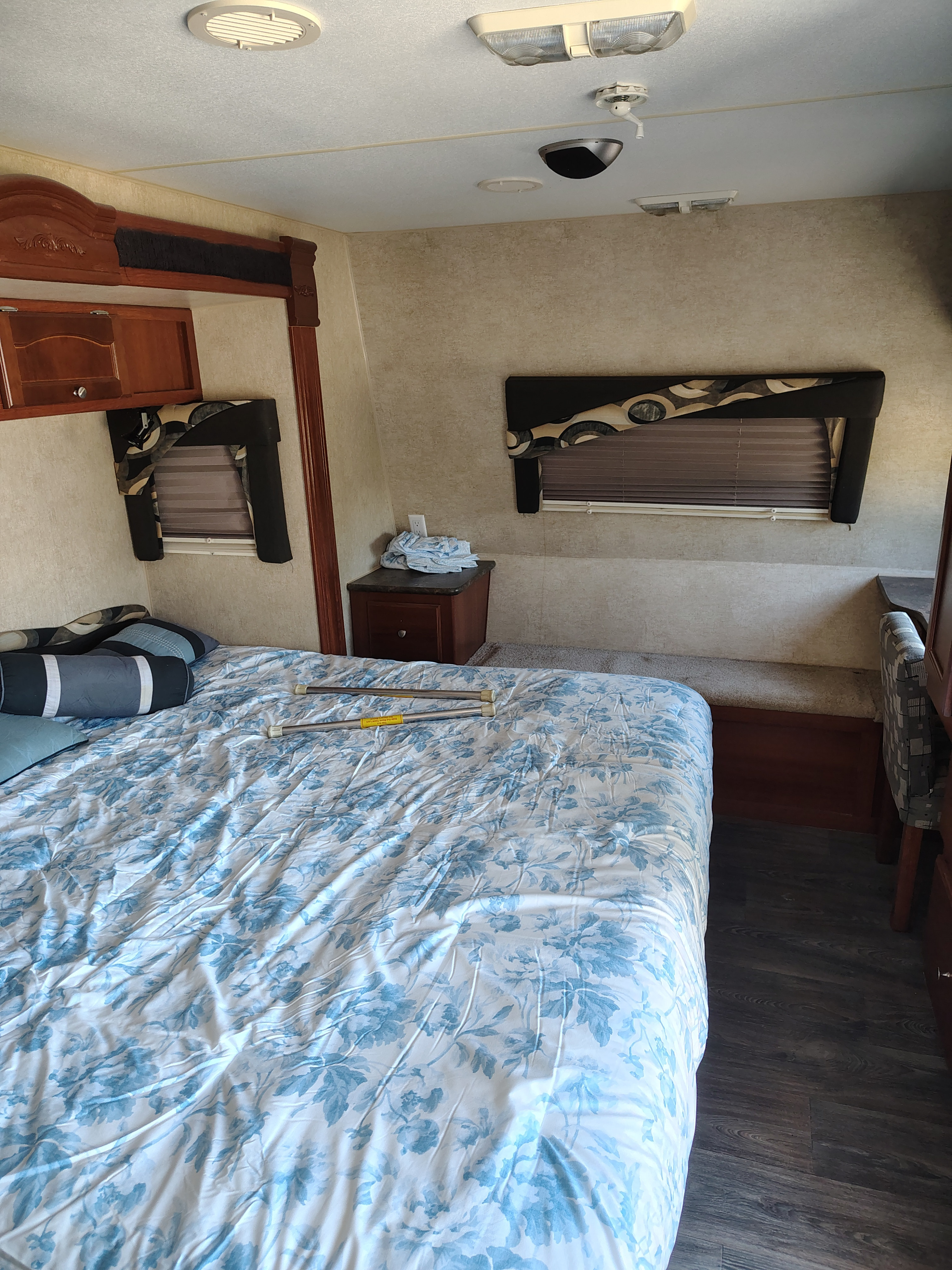 Inside an rv rental: a bedroom with a blue floral bedspread, wood cabinets, and blinds on windows, providing a cozy interior.. Fleetwood Terry 2007