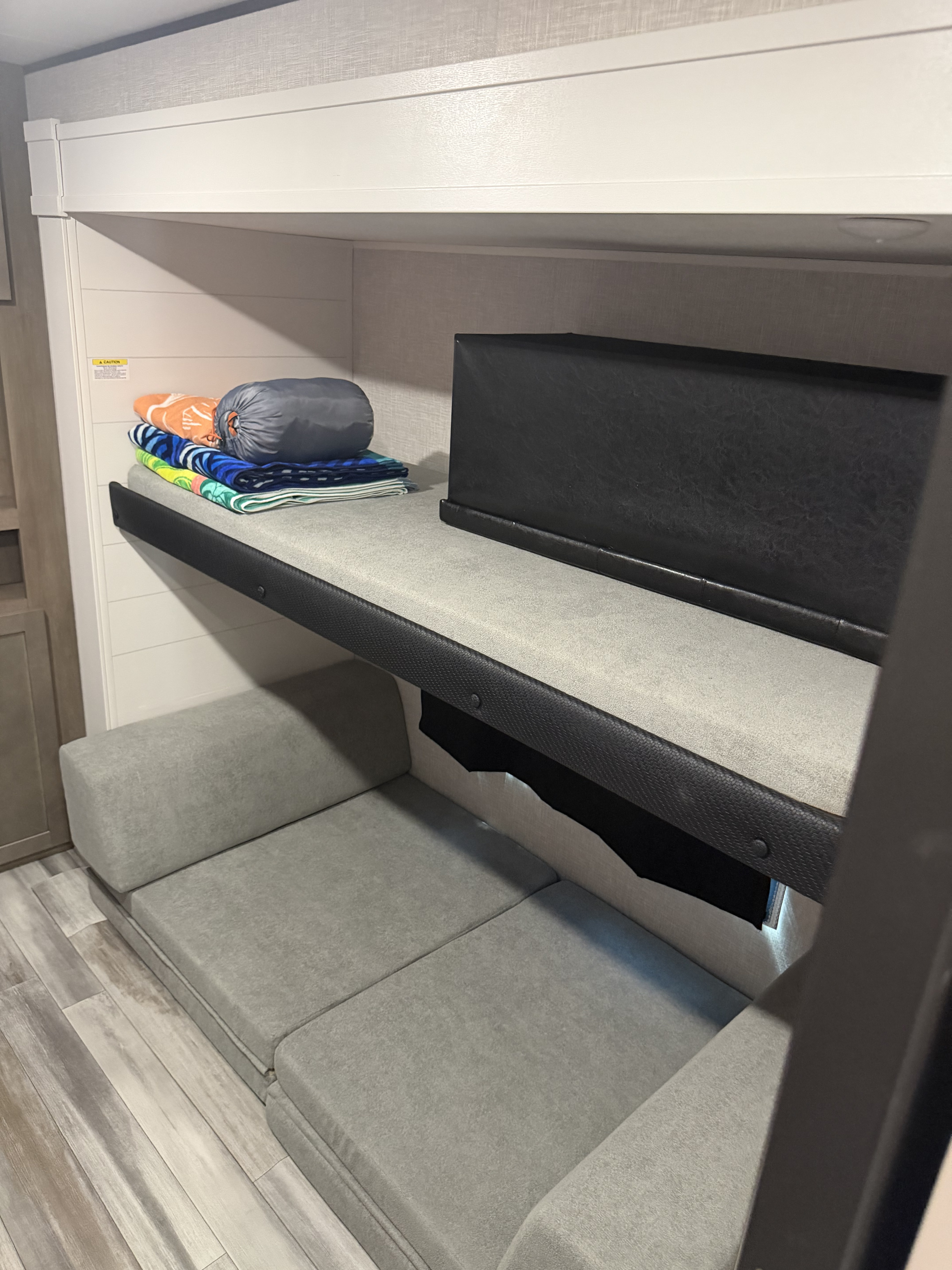 RV rental bunk beds feature cozy upper sleeping with stacked towels & a sleeping bag, plus versatile convertible seating below.. Jayco Jay Flight SLX STX Edition 2025