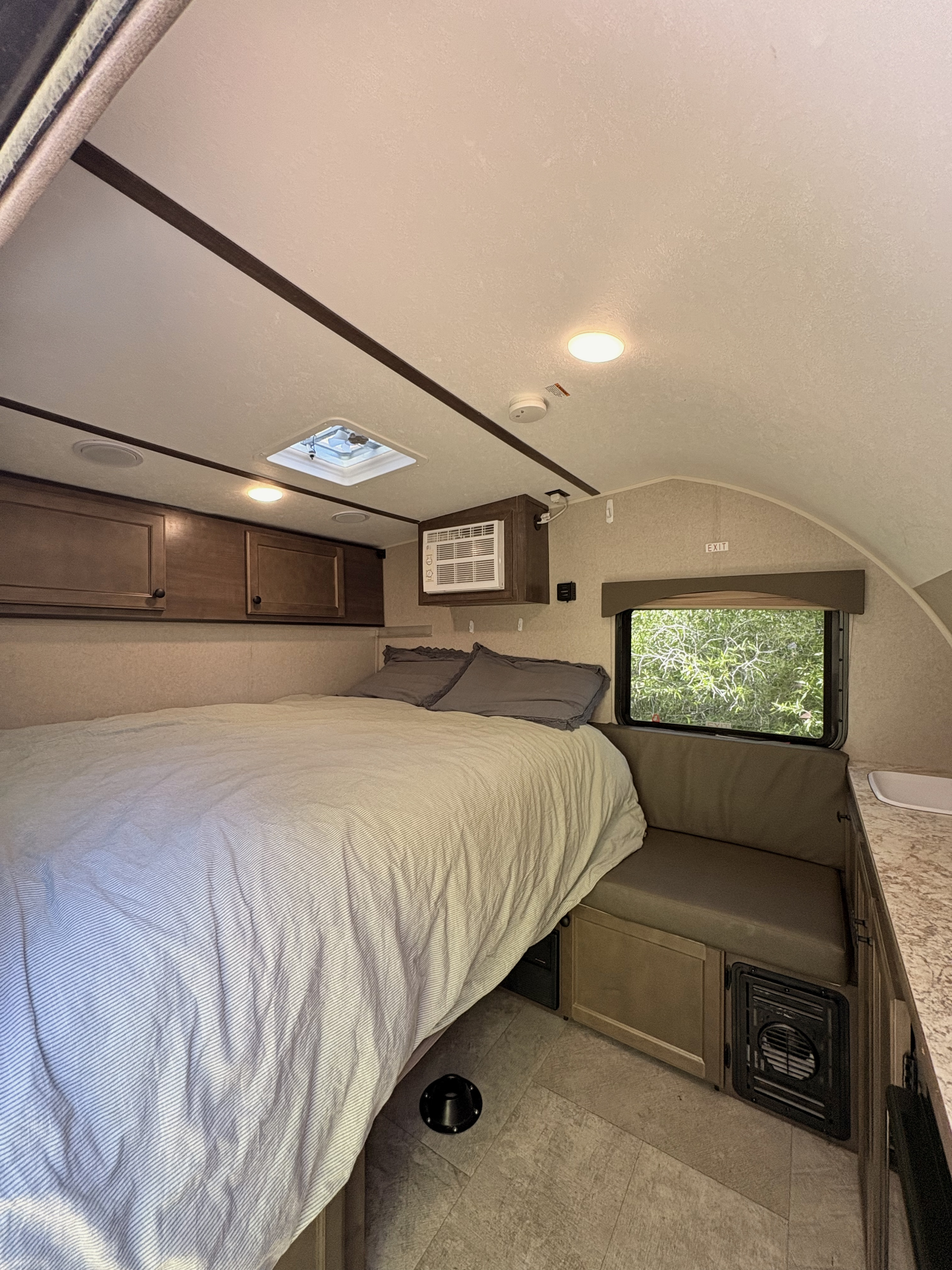 Cozy RV rental interior: a compact bedroom with striped bed, window AC, overhead storage, and floor vent.. Sunset Park RV SunRay 2022