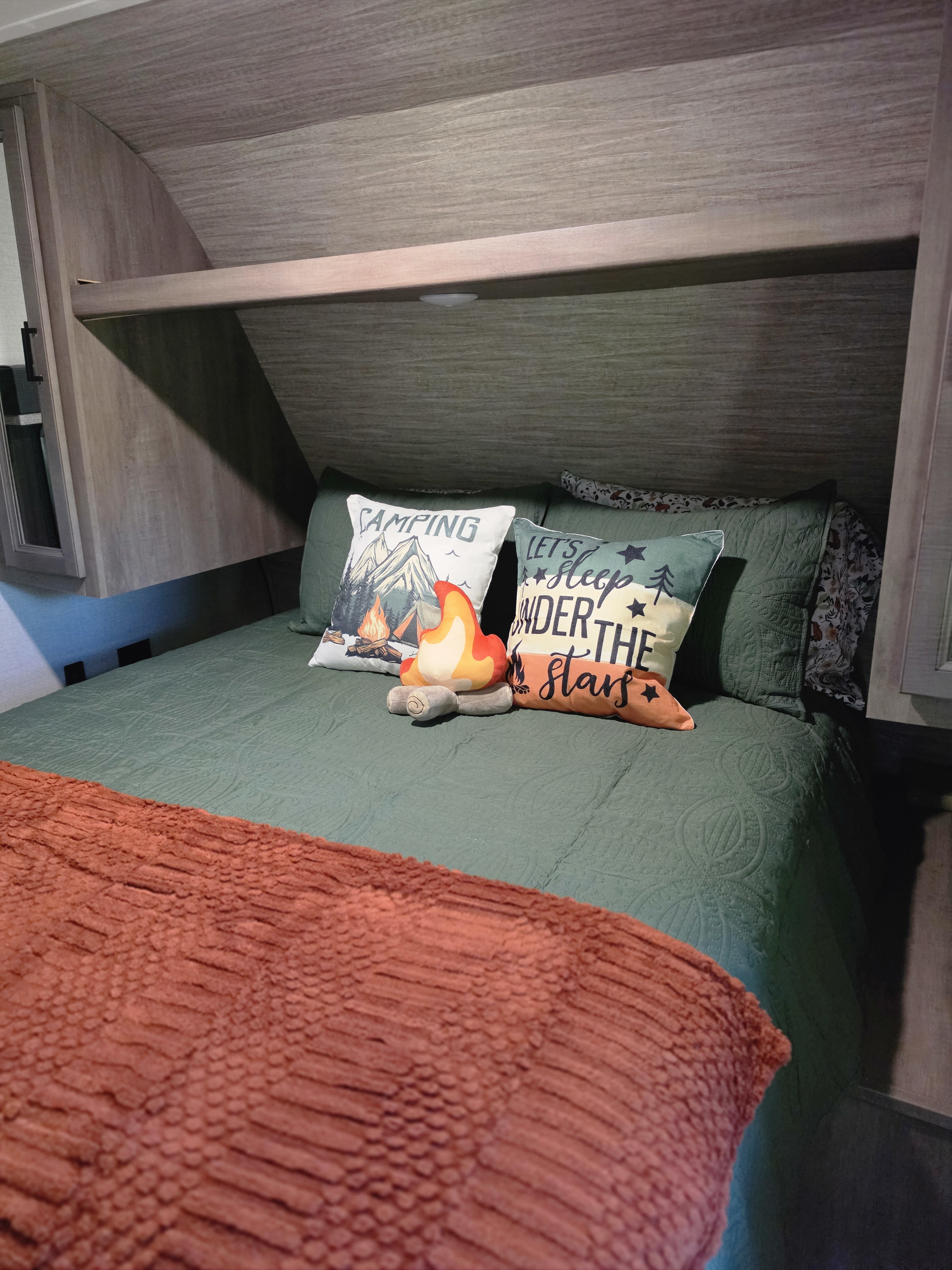 This inviting RV rental bedroom has a bed with green bedding, an orange throw, and charming camping pillows.. Starcraft Autumn Ridge 2022