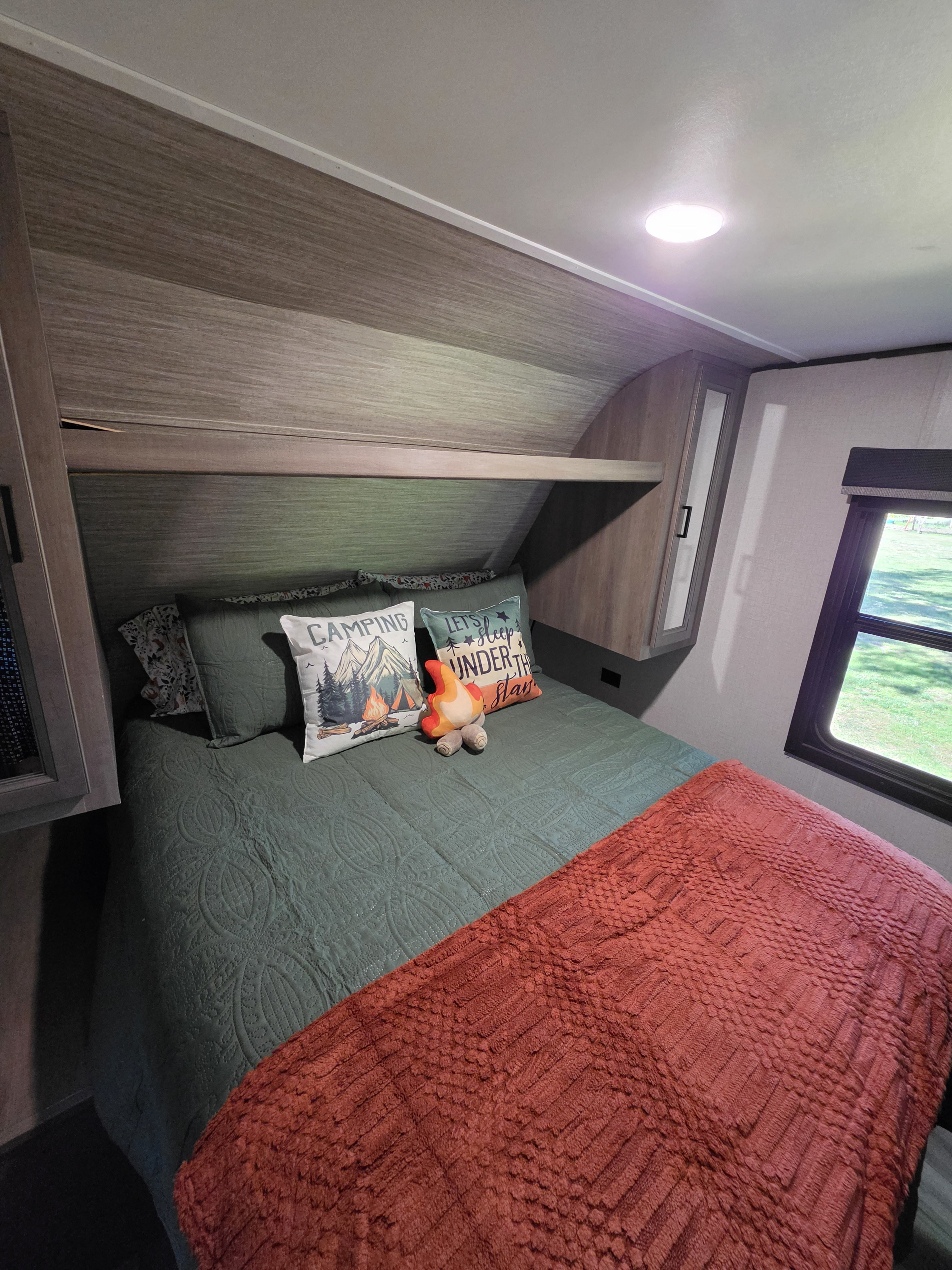 Cozy RV rental bedroom with camping-themed pillows, green bedding, and an orange blanket, ideal for travel.. Starcraft Autumn Ridge 2022