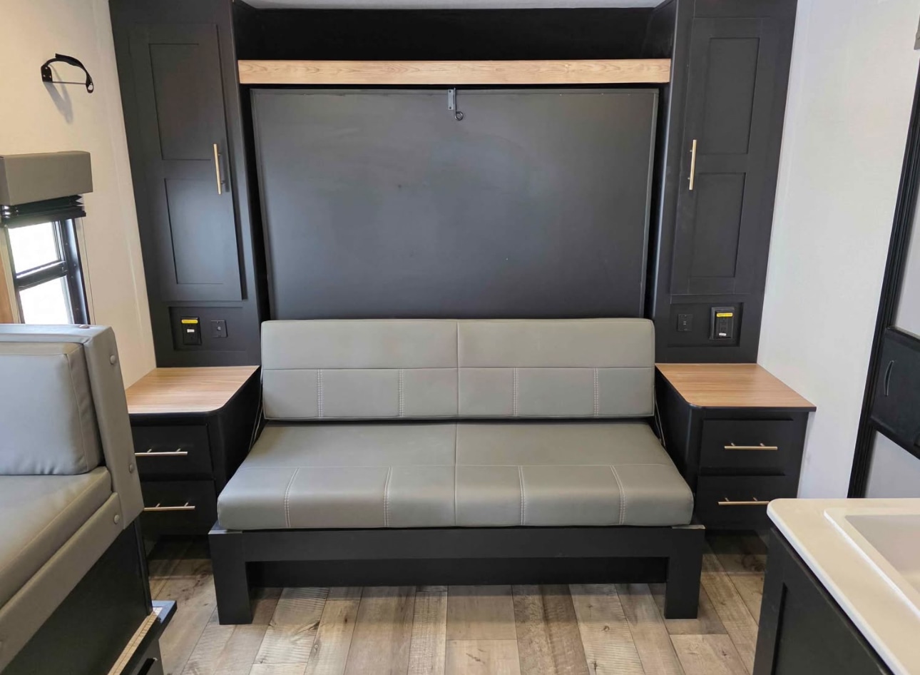 RV rental's modern interior: gray sofa, folded wall bed, black cabinets with wood accents and built-in storage.. Keystone RV Springdale 2023