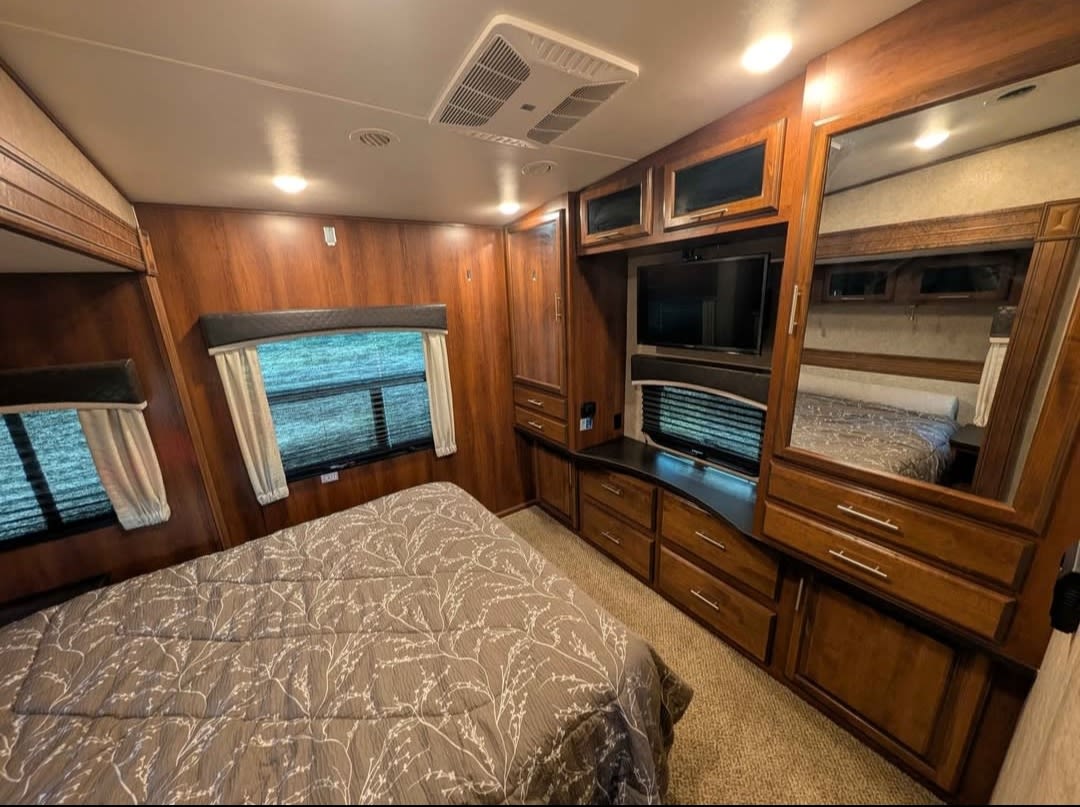 Cozy RV rental bedroom with warm wood interiors, comfortable bed, TV, and ample storage for your next adventure.. Jayco Eagle 2018